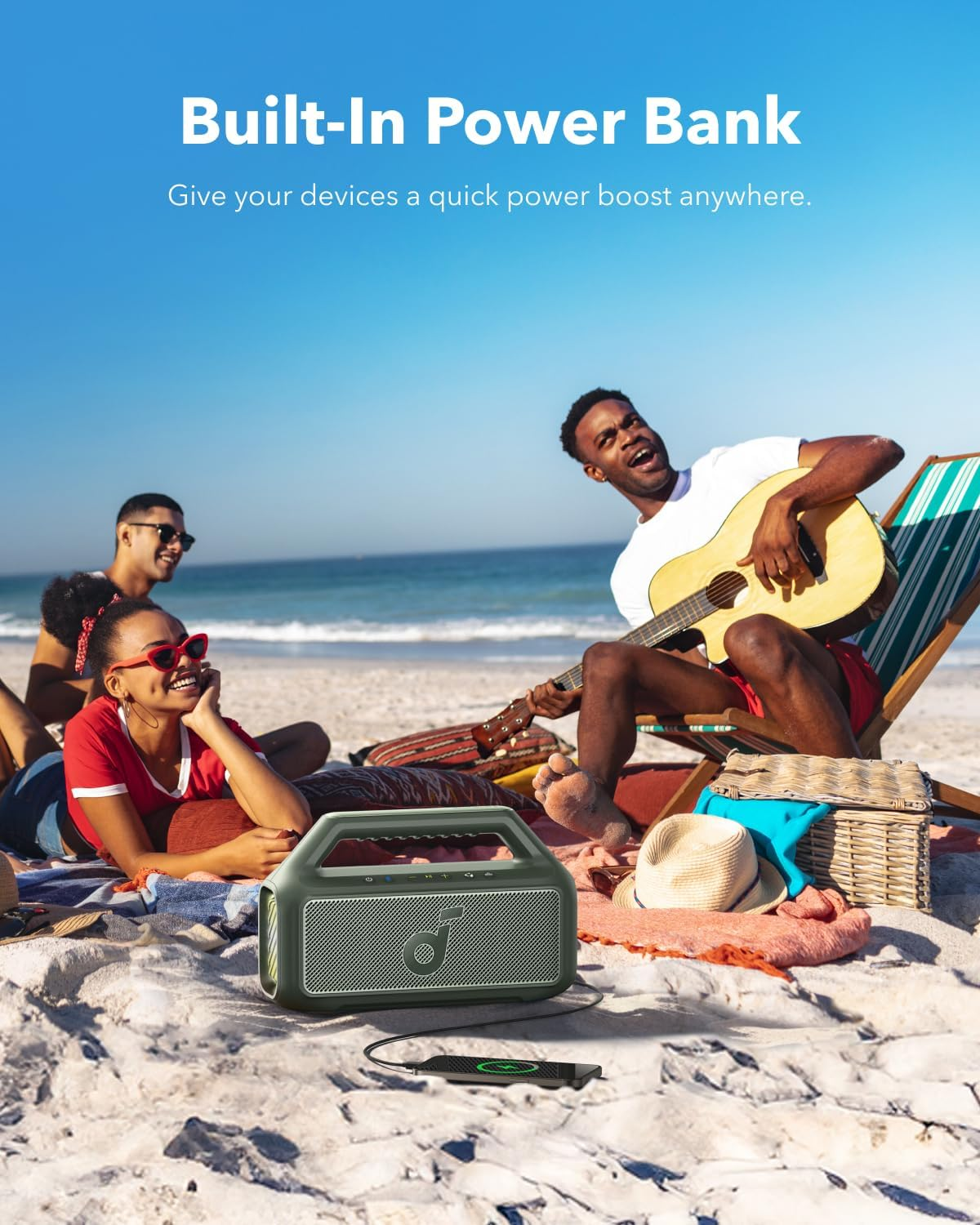Plaj sahnesi: İnsanlar ve hoparlör. Gitar çalan adam. Metin: Power Bank.