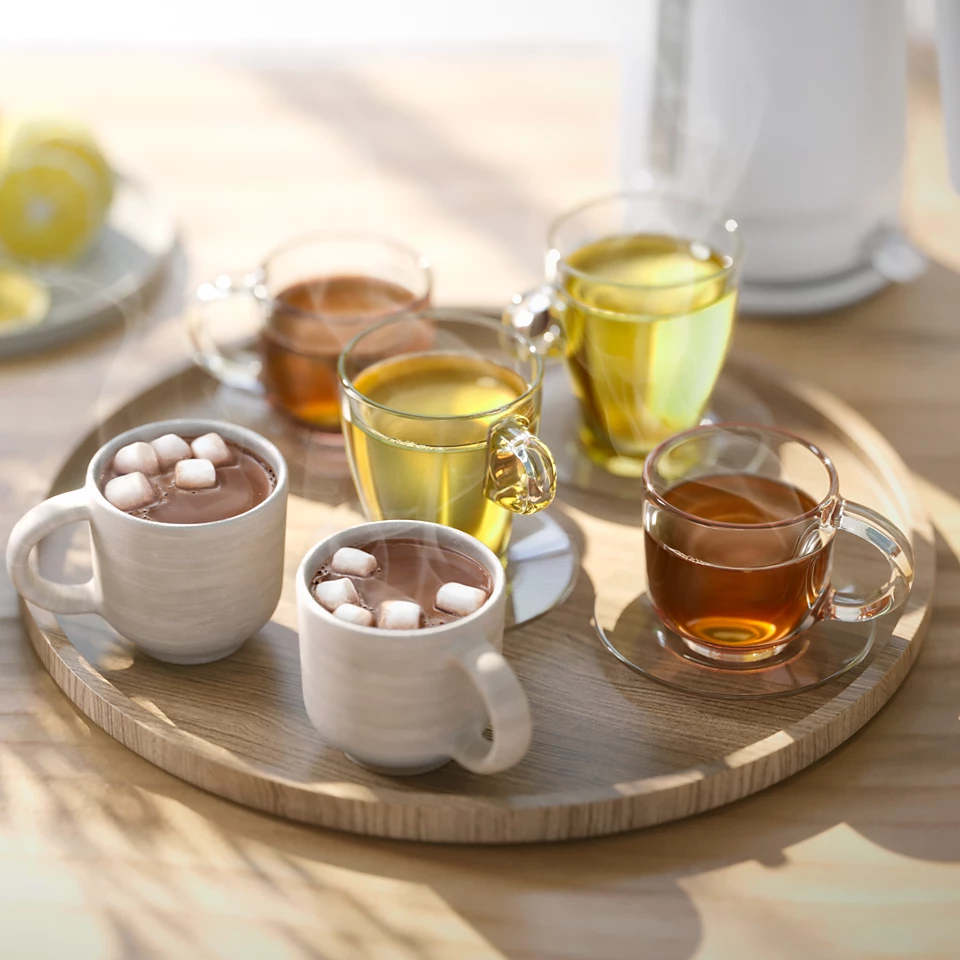 Egy fa tálcán két bögre forró csokoládé mályvacukorral és négy csésze tea található.