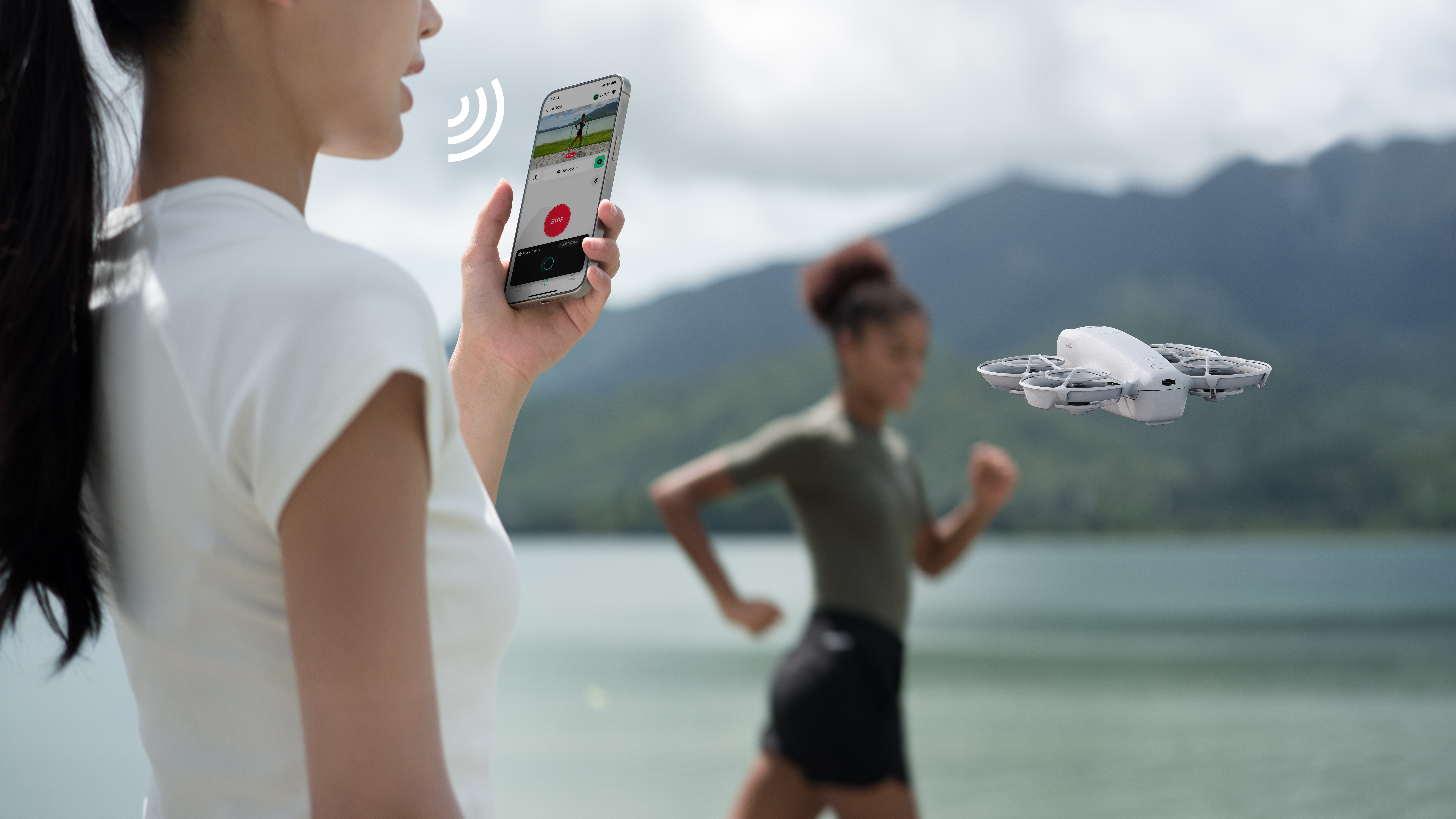 Kobieta trzymająca telefon, dron w locie i kolejna kobieta biegnąca w malowniczej scenerii na zewnątrz.