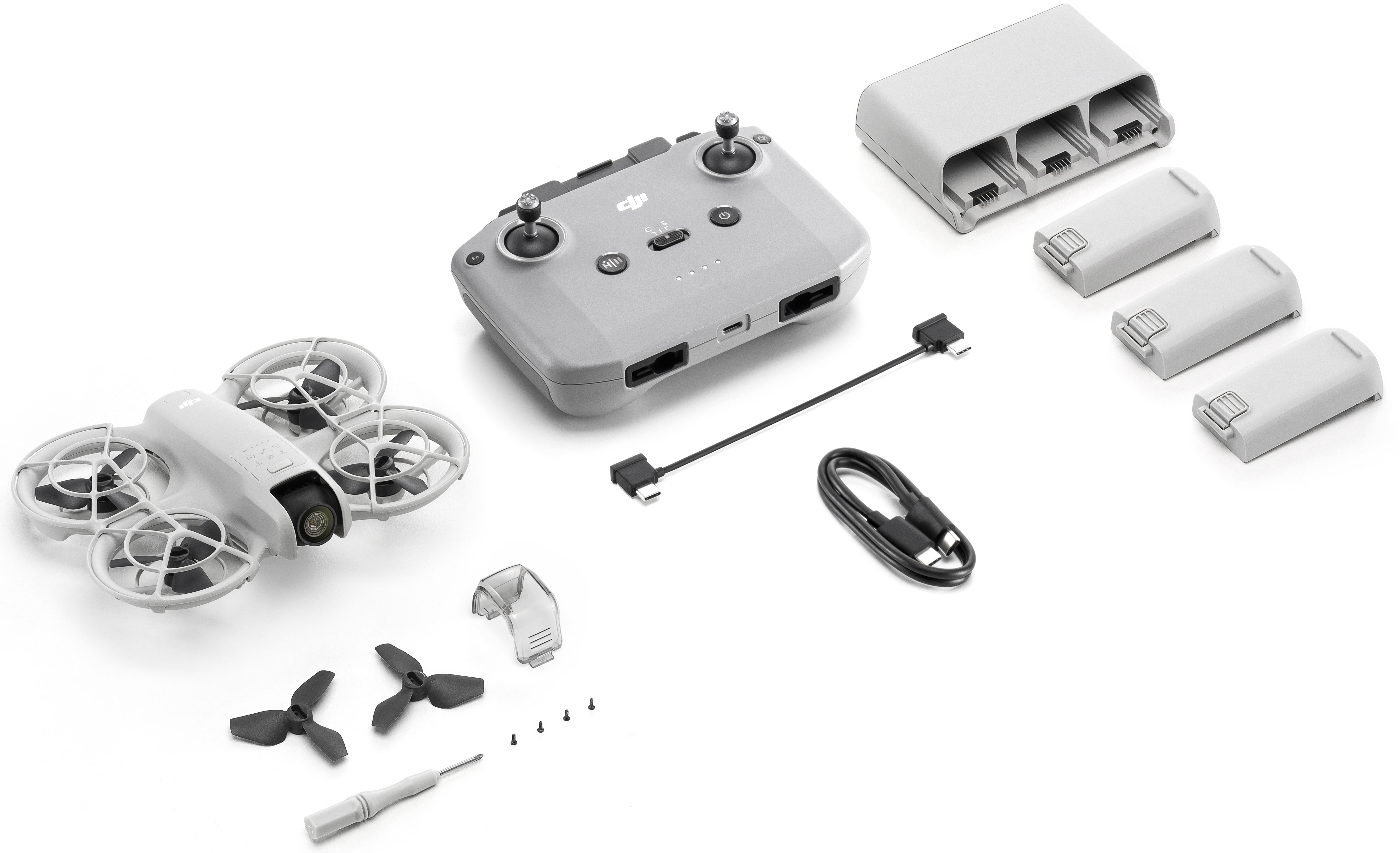 Biały dron z pilotem, bateriami i ładowarką na białej powierzchni. Czarne śmigła.