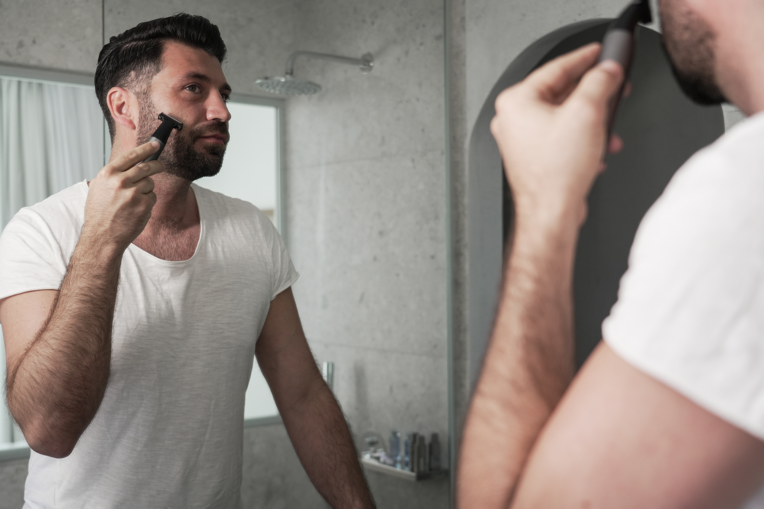 Hombre afeitándose en el espejo del baño. El reflejo muestra la acción.