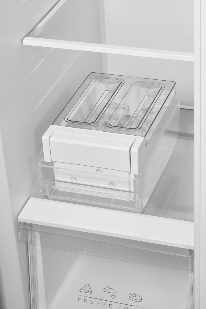 À l'intérieur d'un réfrigérateur, une machine à glaçons en plastique transparent avec deux compartiments se trouve au-dessus du congélateur.