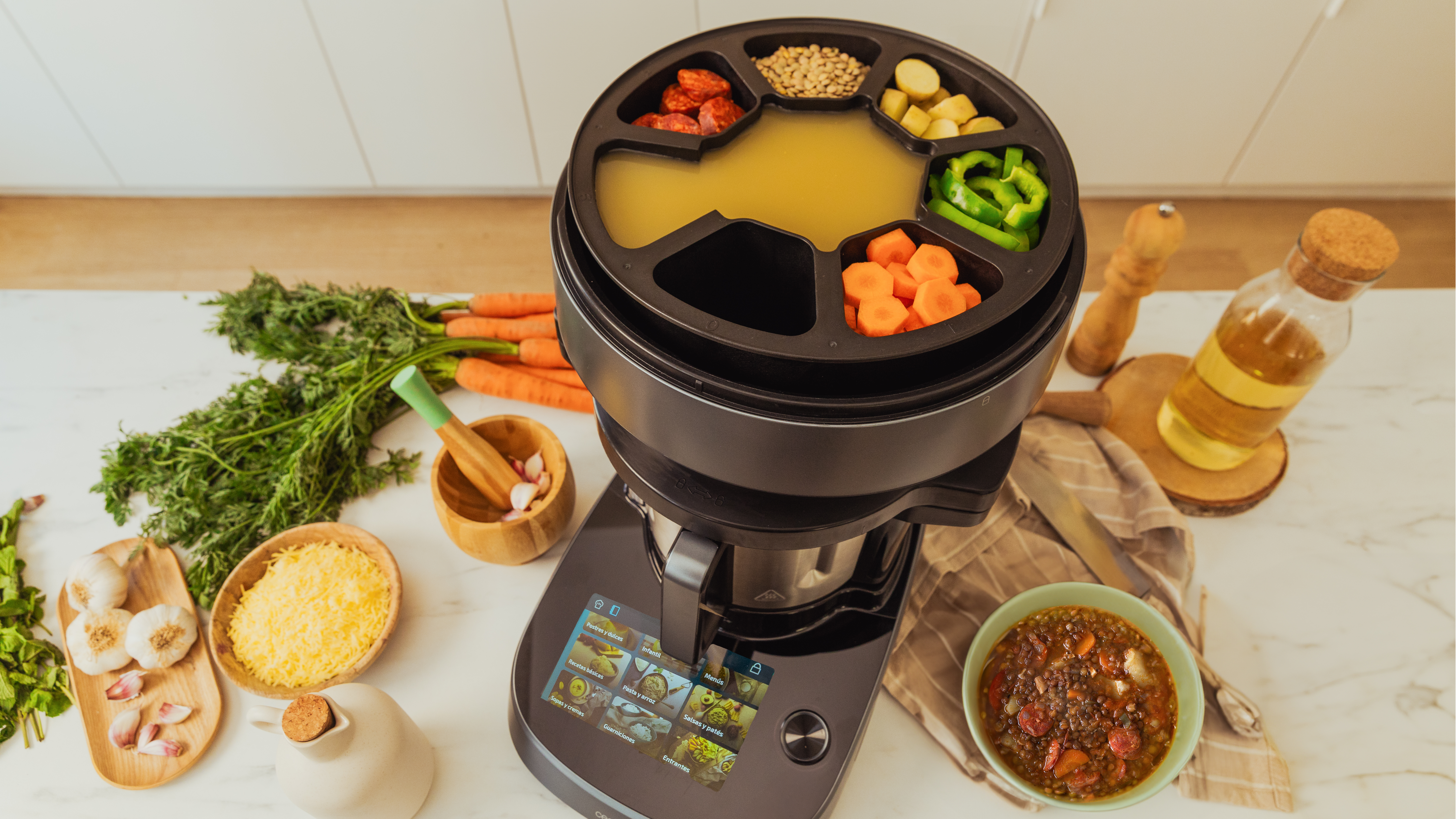 Un dispositivo de cocina con ingredientes en una superficie blanca: verduras, aceite y ajo.