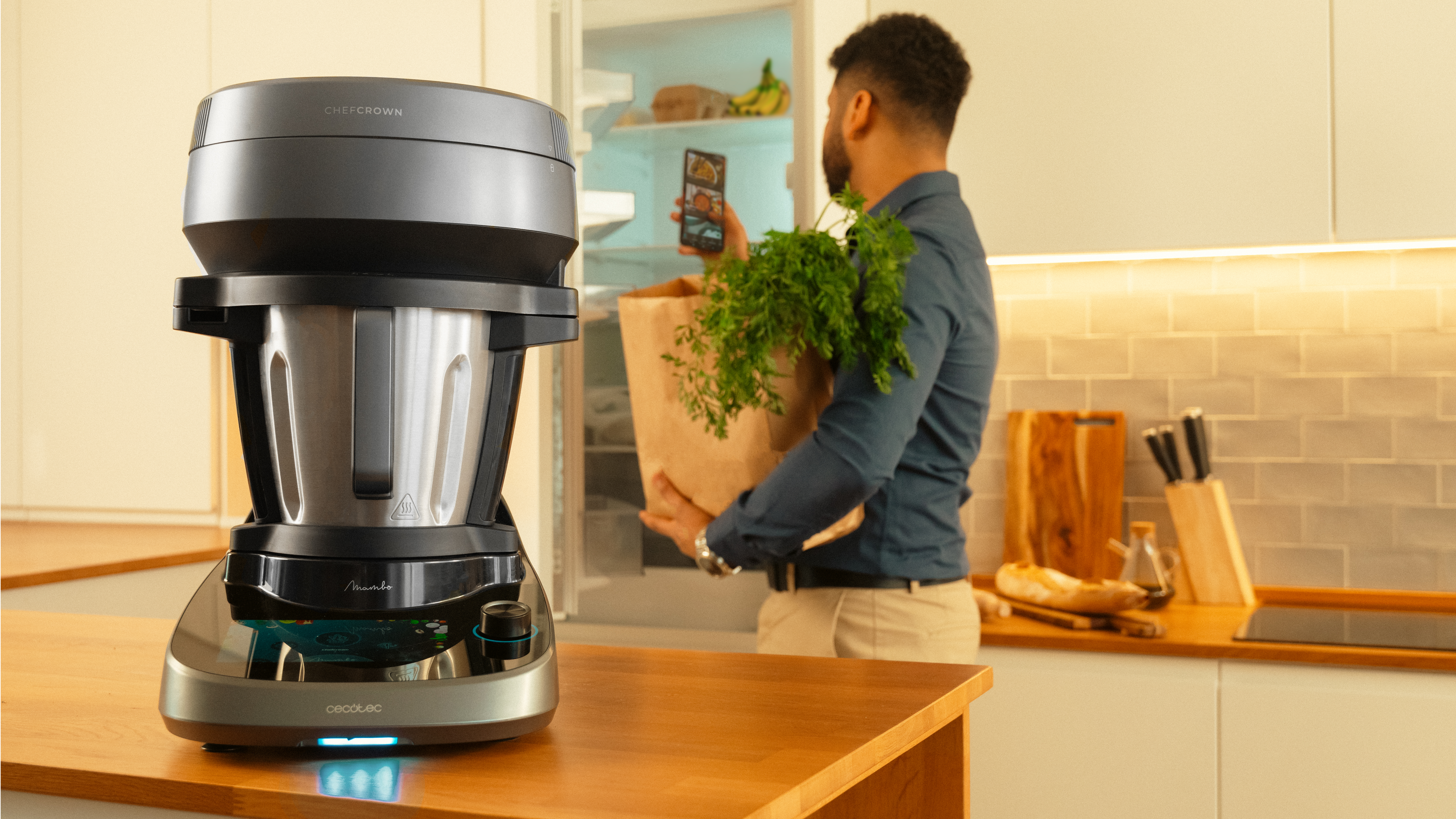 Hombre sosteniendo comestibles, cerca de una cocina con un procesador de alimentos.