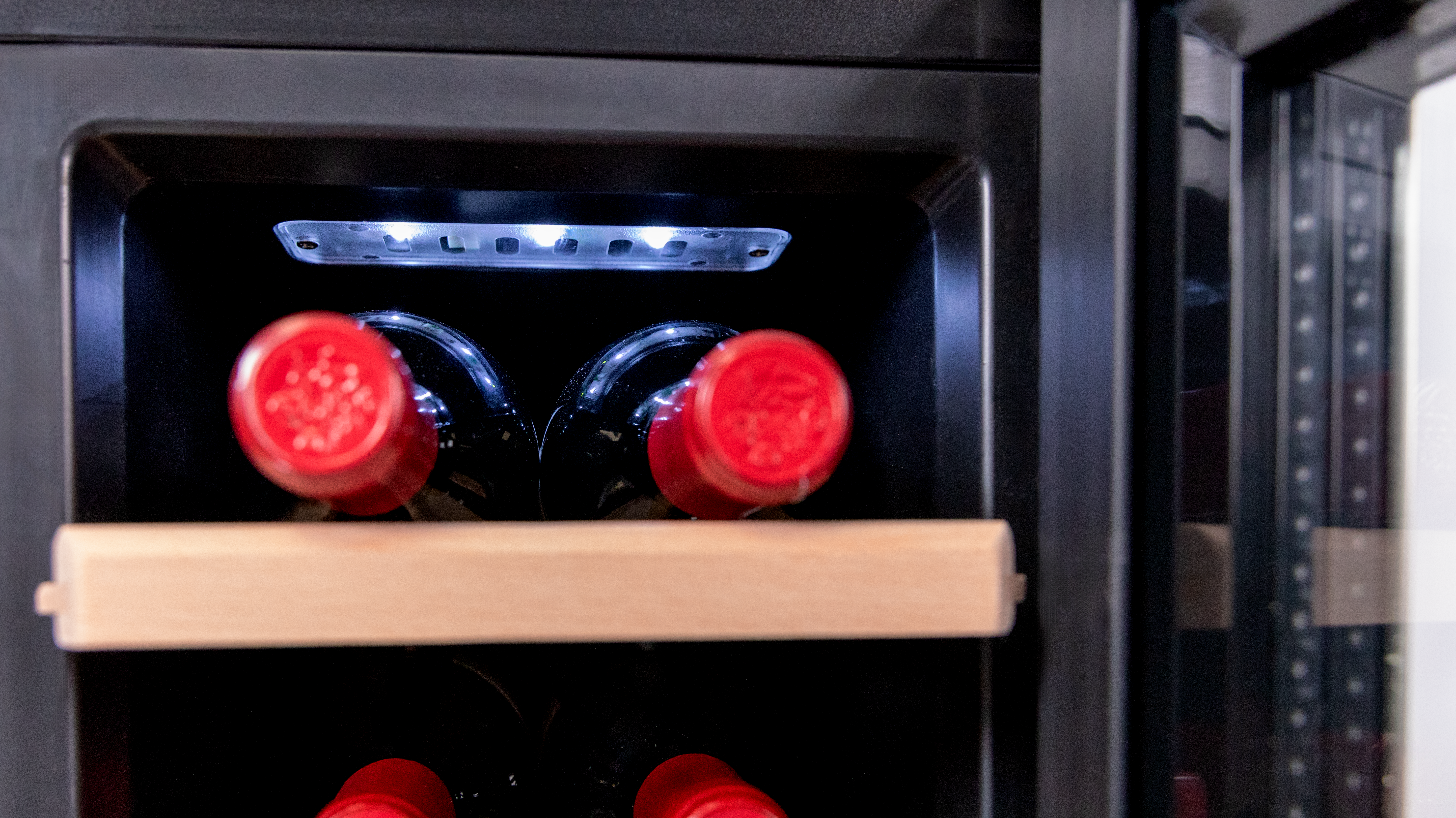 Interior de una vinoteca con botellas y tapas rojas, iluminadas por luces LED.