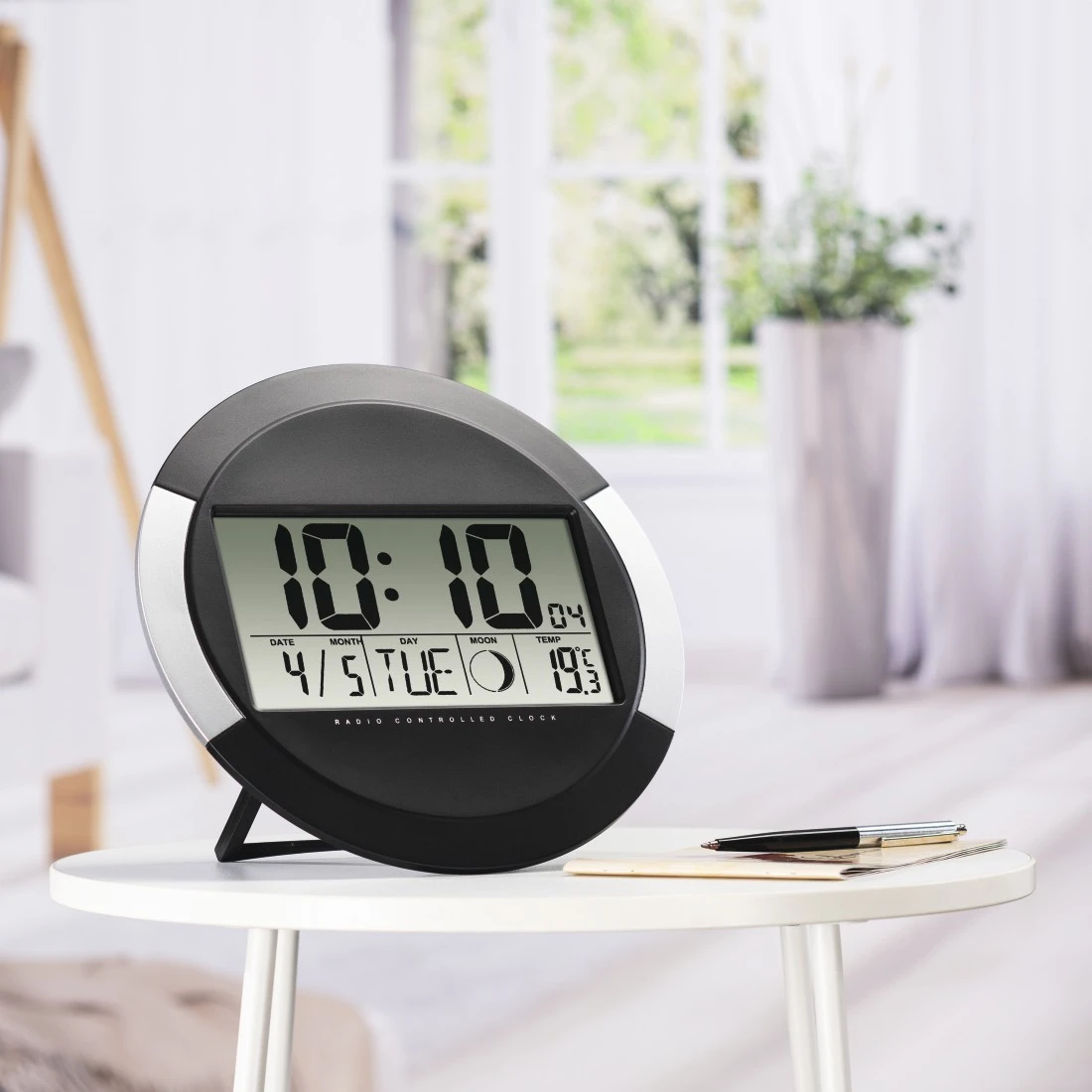 Un orologio digitale che mostra le 10:10 con data e temperatura su un tavolo bianco.
