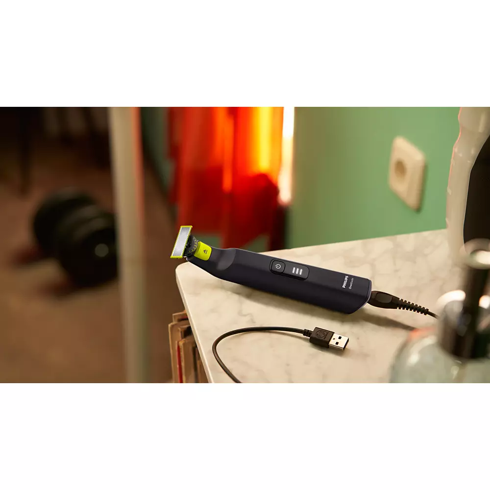 Schwarzer und grauer Barttrimmer mit USB-Kabel auf einem Tisch. Hintergrund zeigt Raum.