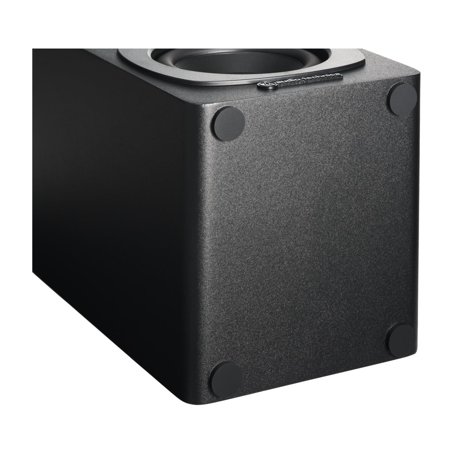 Subwoofer nero, quadrato con angoli arrotondati e piedini in gomma. Messa a fuoco sulla superficie strutturata.