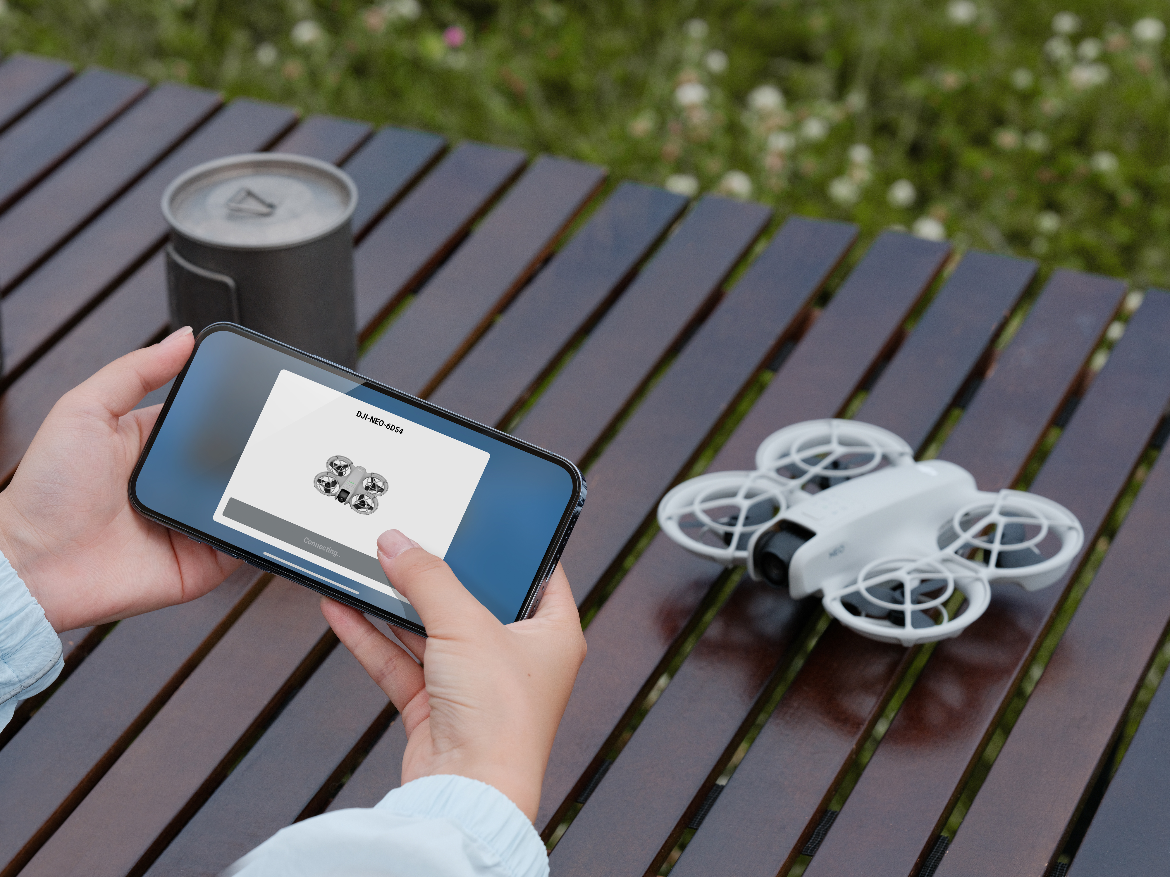 Personne tenant un téléphone avec une image de drone, un drone à côté.