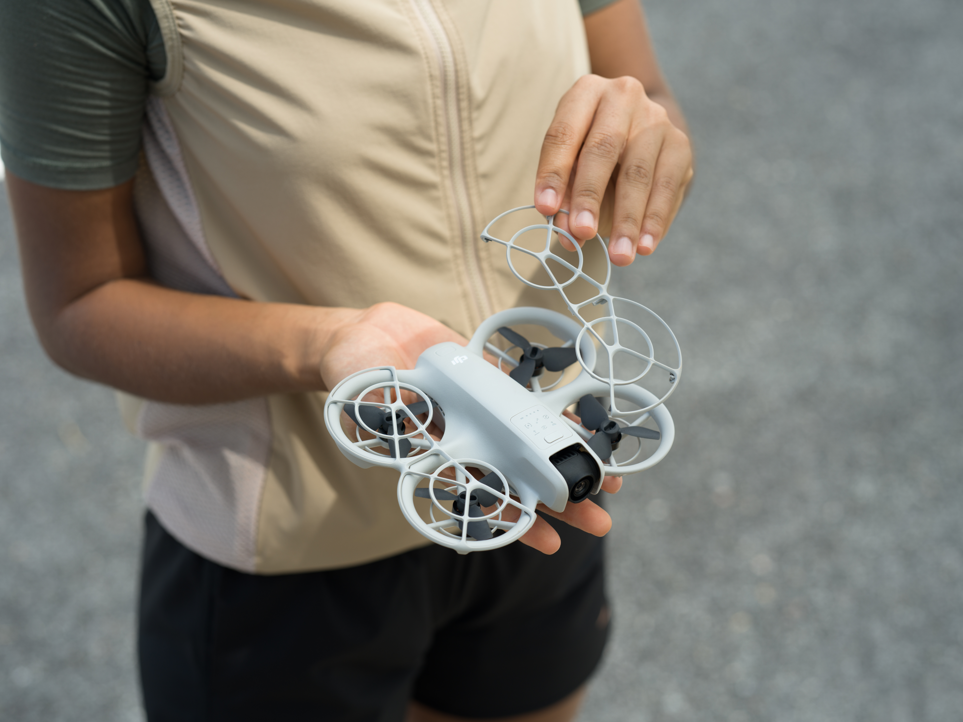 Personne tenant un petit drone gris. Le drone a des anneaux de protection autour des hélices.