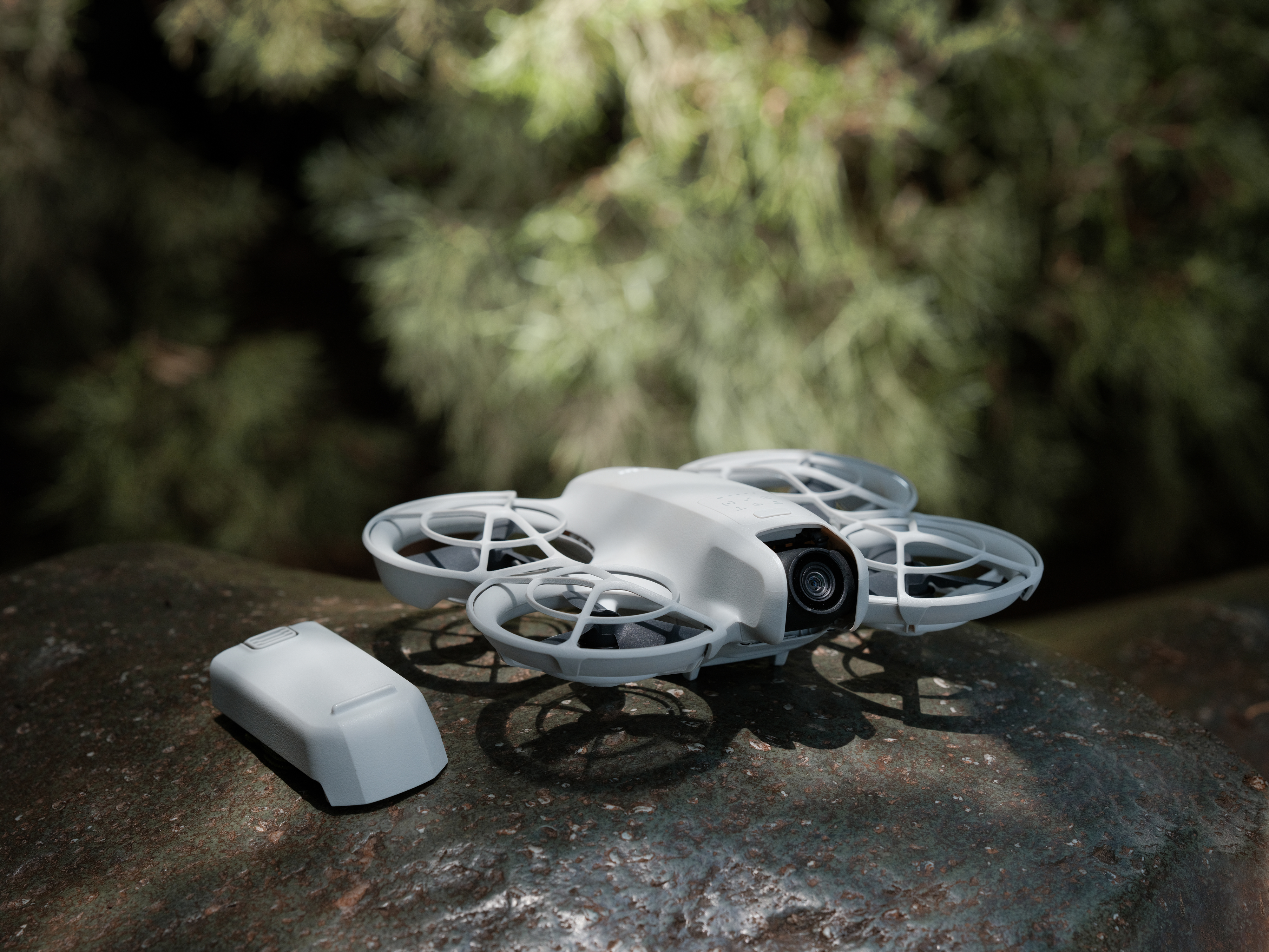 Drone blanc avec quatre hélices et batterie reposant sur une pierre.
