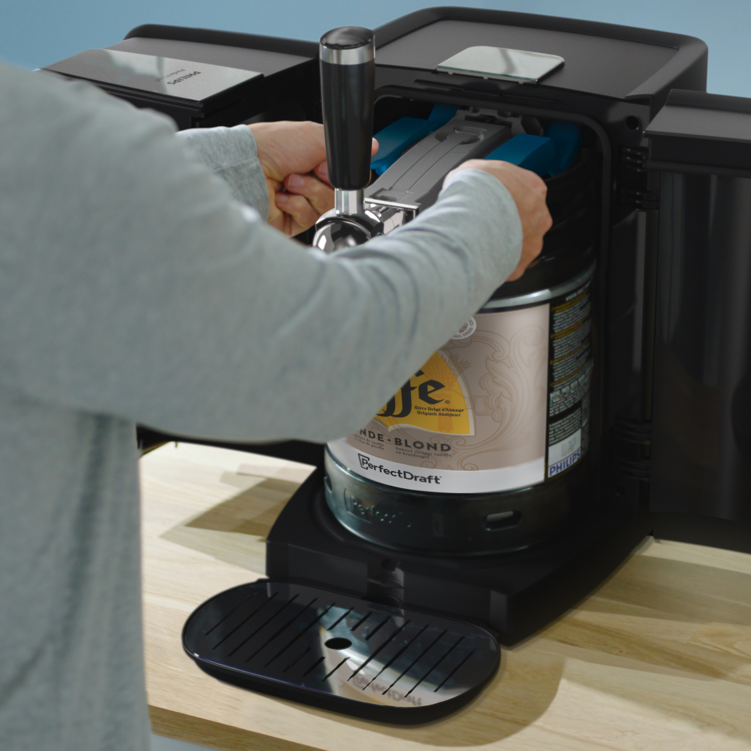 Persoon plaatst een biervat in een zwarte PerfectDraft machine, op een houten oppervlak.