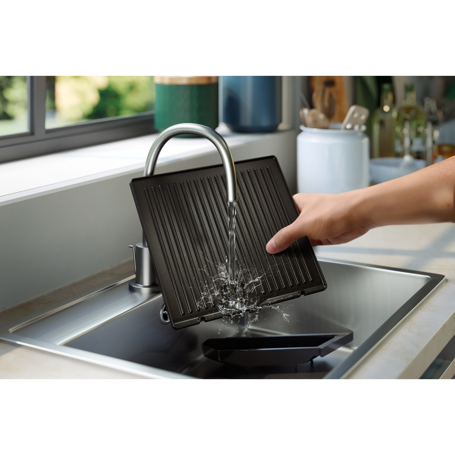 Een zwarte grillpan wordt onder een kraan gewassen. Er spat water.