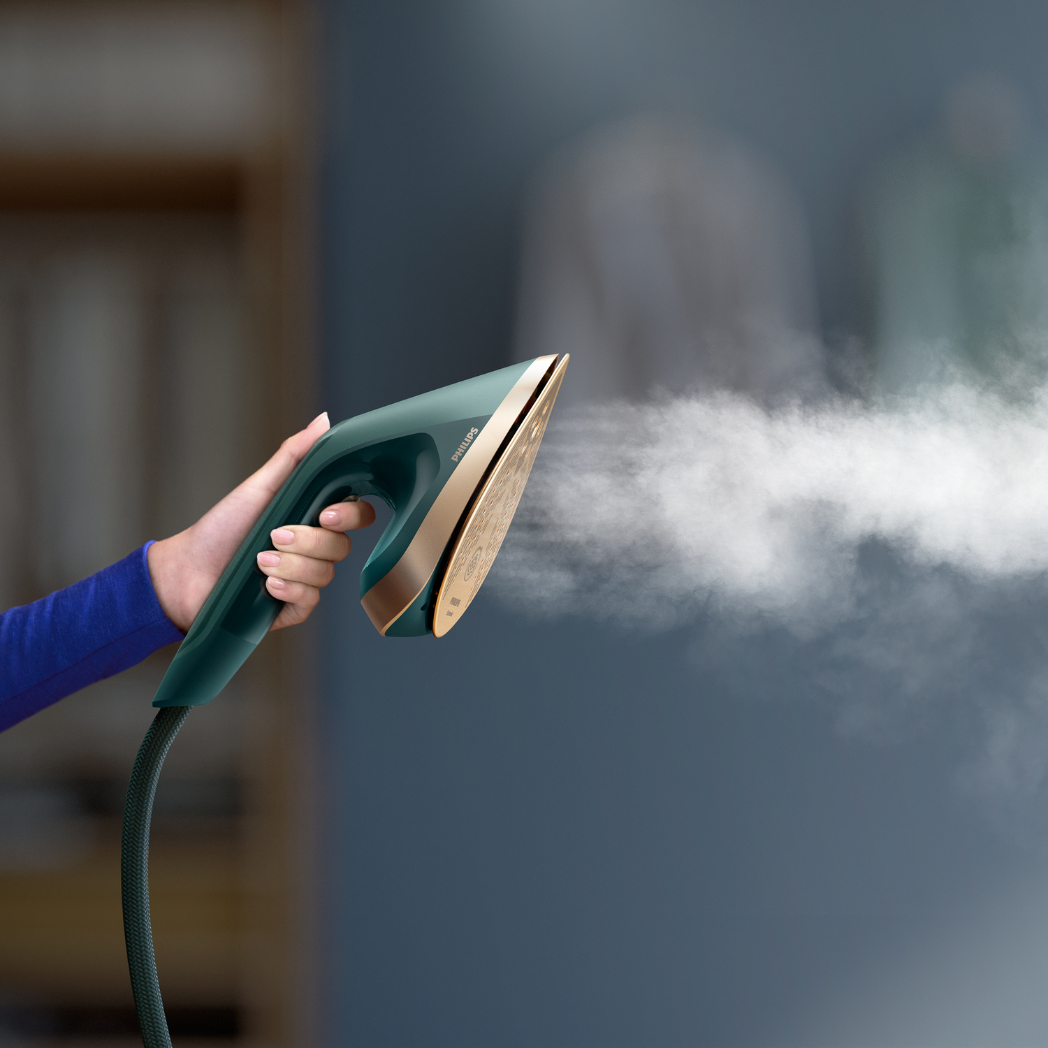 Une personne repassant des vêtements avec un fer Philips vert d'eau et doré, dégageant de la vapeur.