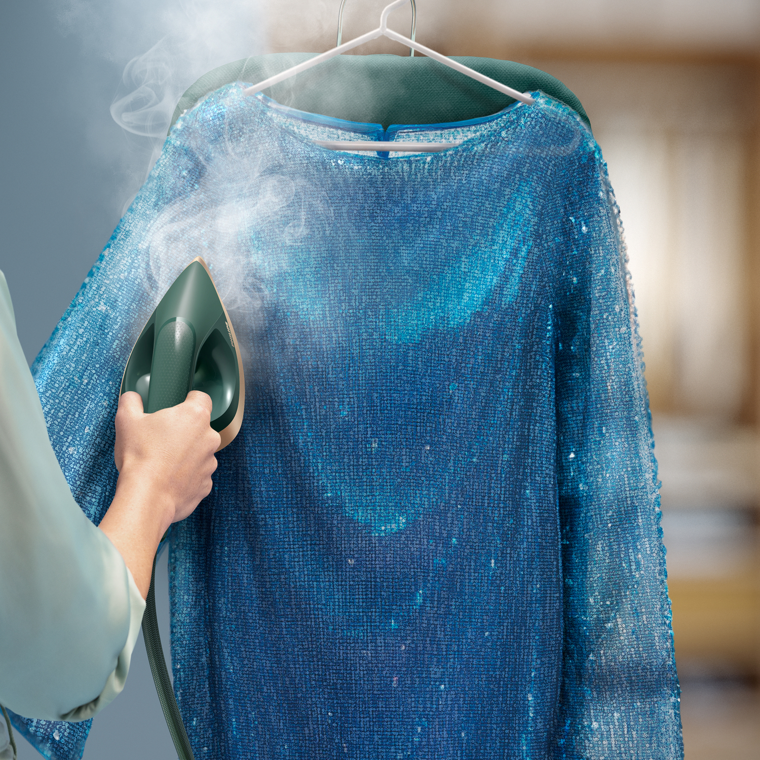 Une personne repassant une robe bleue à sequins avec un fer à repasser vert.