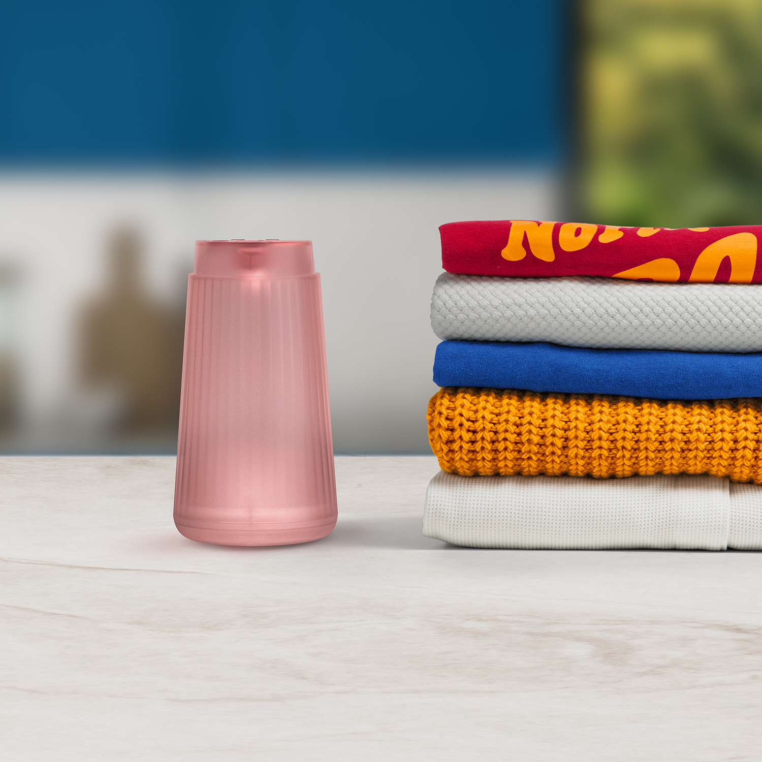 A pink air freshener next to a stack of folded clothes on a white table. Blurred background.