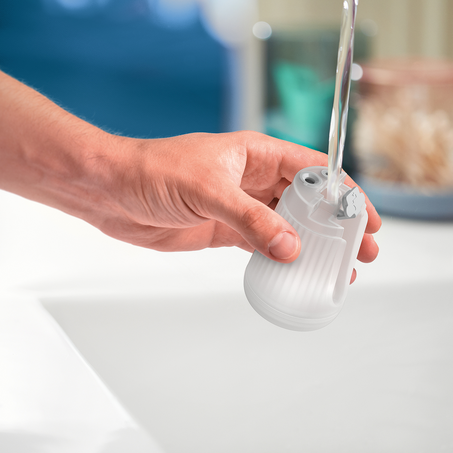 Hand holding a white pencil sharpener over a sink with running water. White background.