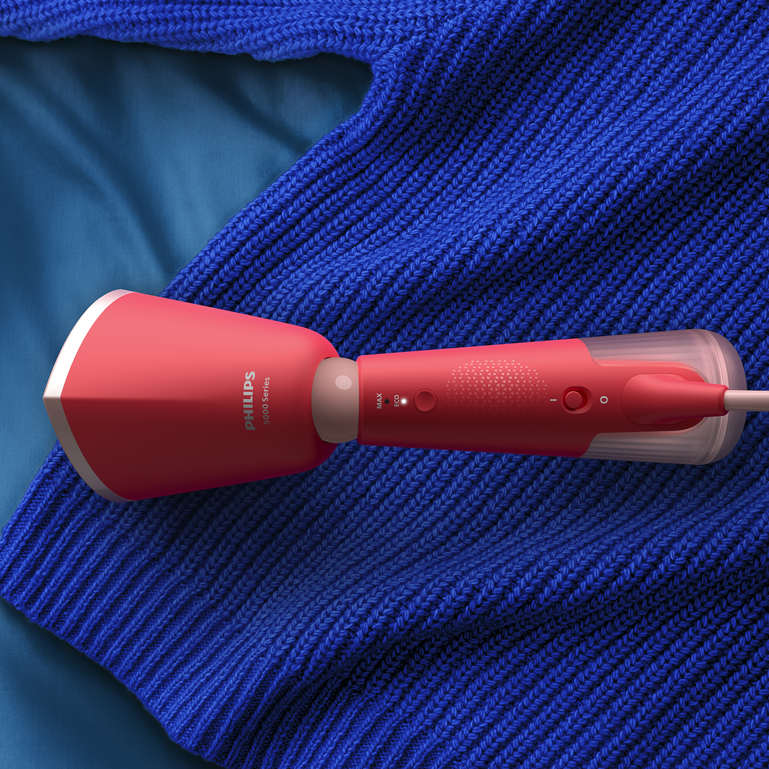 Red Philips steamer on blue sweater. Steamer angled with handle and cord.