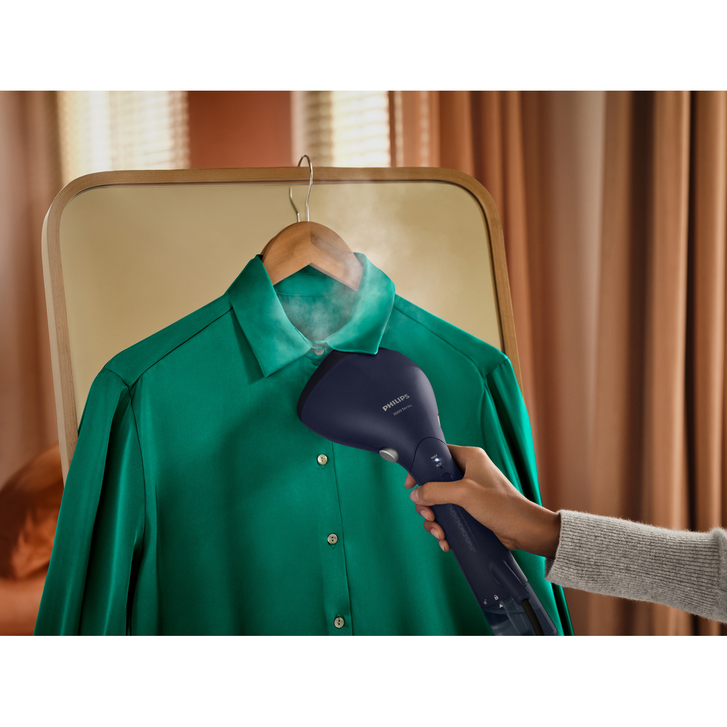 Hand steaming a green shirt with a blue Philips steamer.