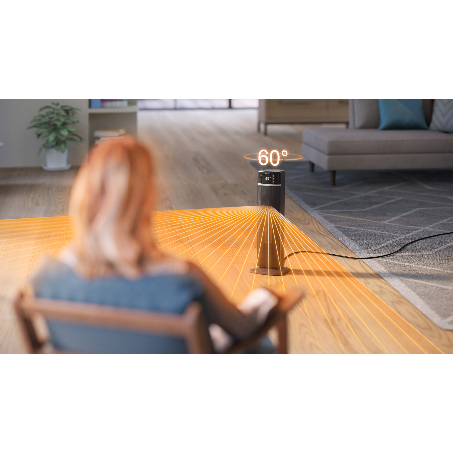 A woman sits near a heating fan that emits warm air. The fan is on a wooden floor.