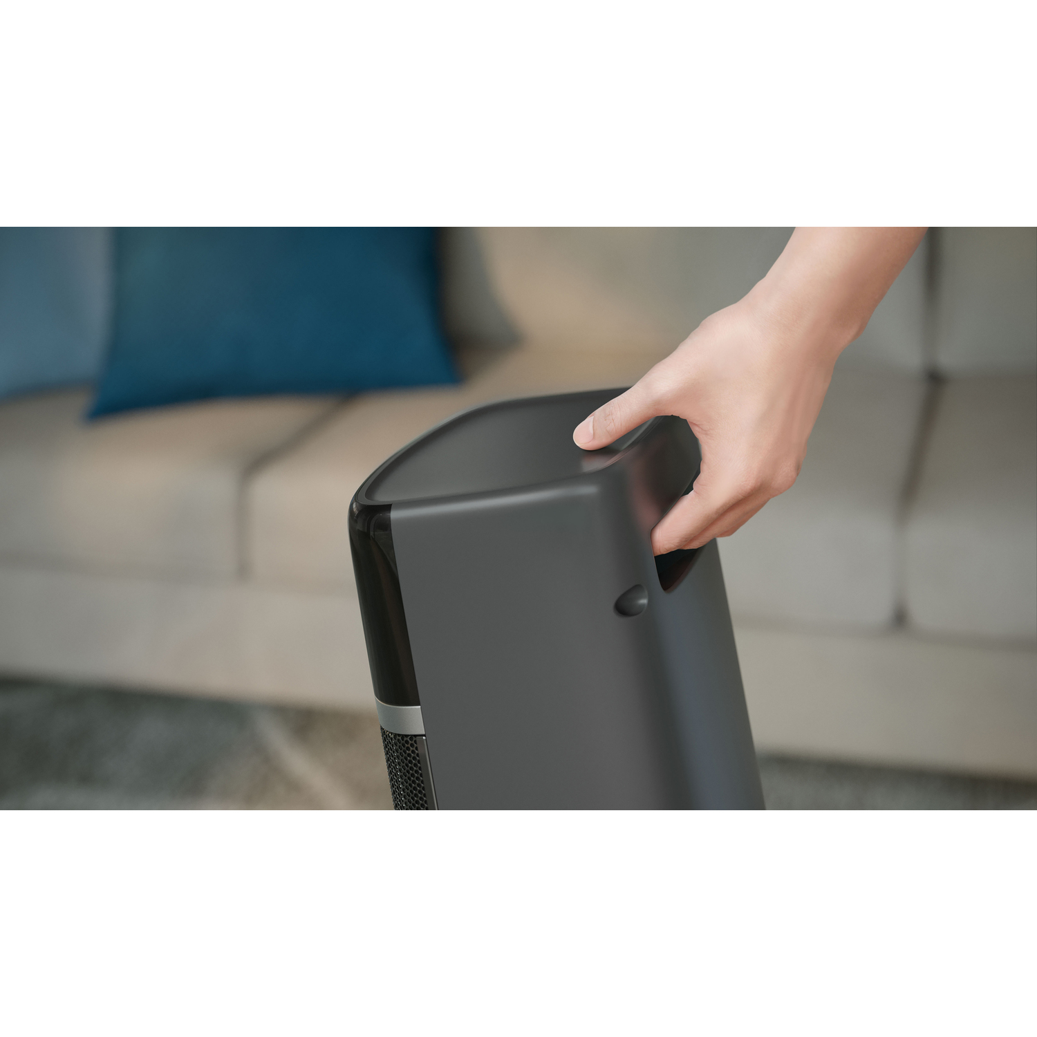Hand holding a black air purifier in a home setting.