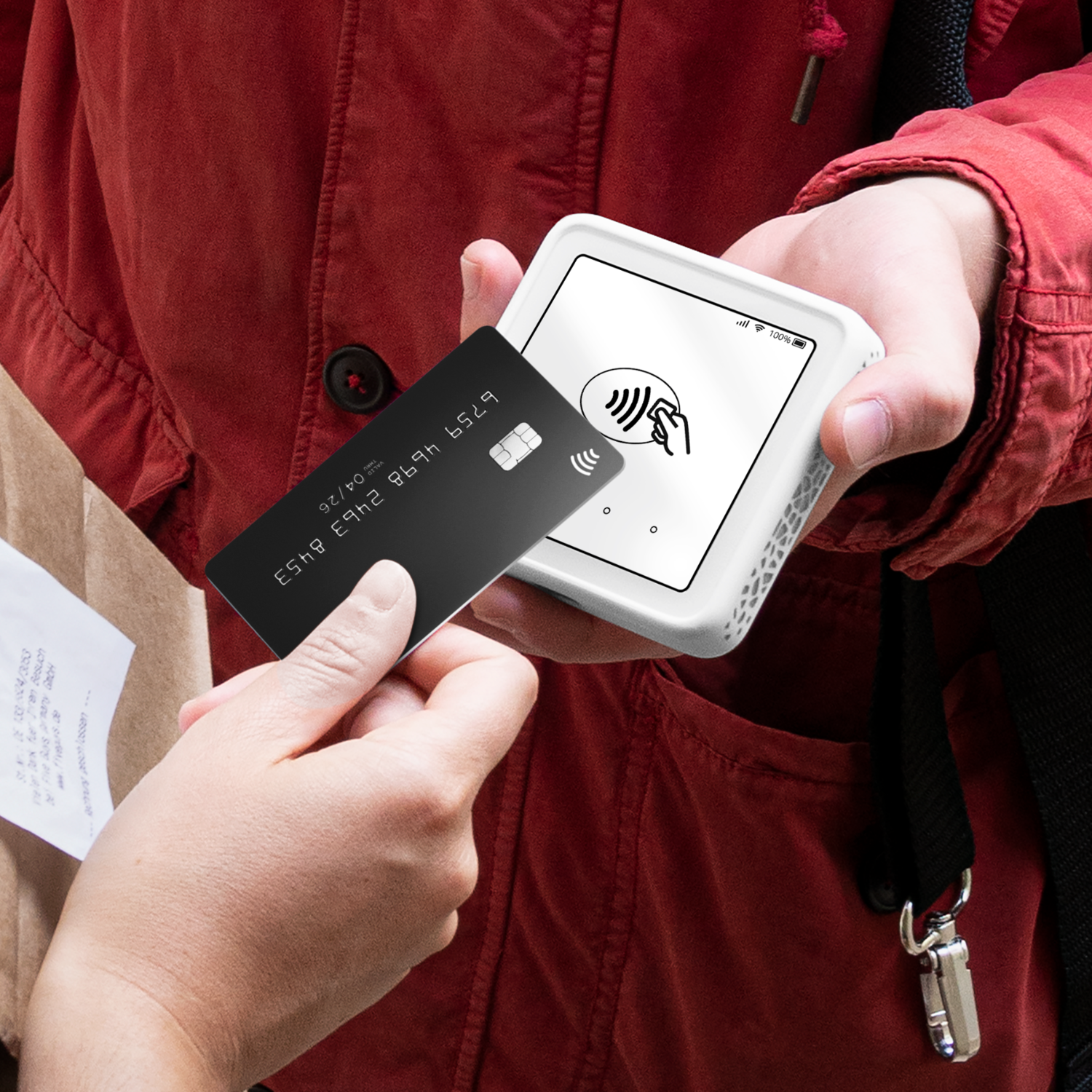 A person's hand holds a black credit card near a card reader. The reader displays a payment symbol.