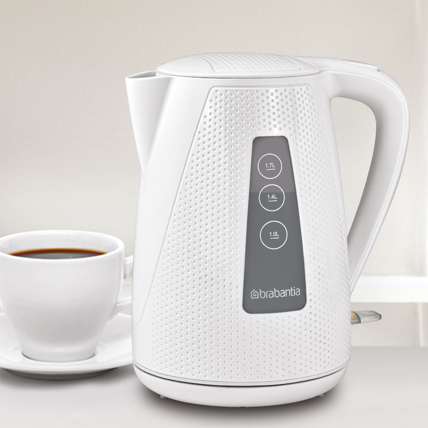White kettle with a cup of coffee. The kettle shows water levels and the brand name Brabantia.