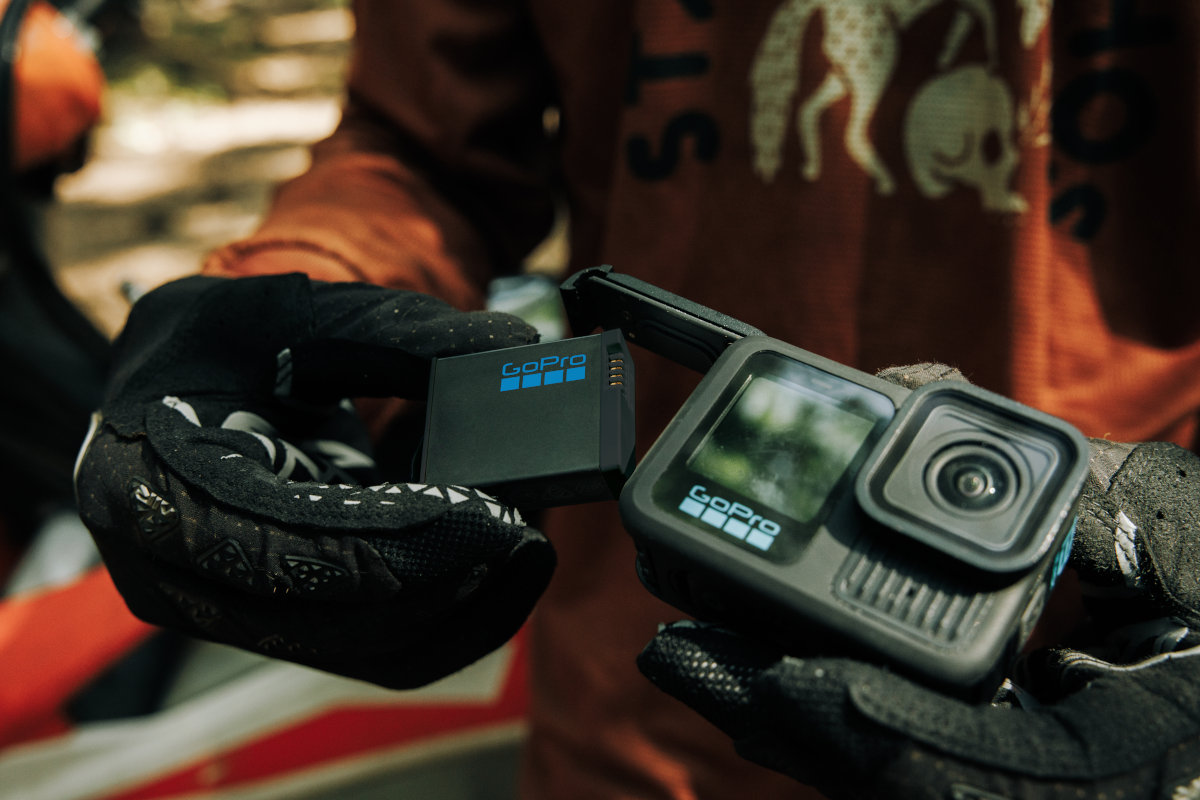 Ręce trzymające kamerę GoPro i jej akumulator. Noszone są czarne rękawice.