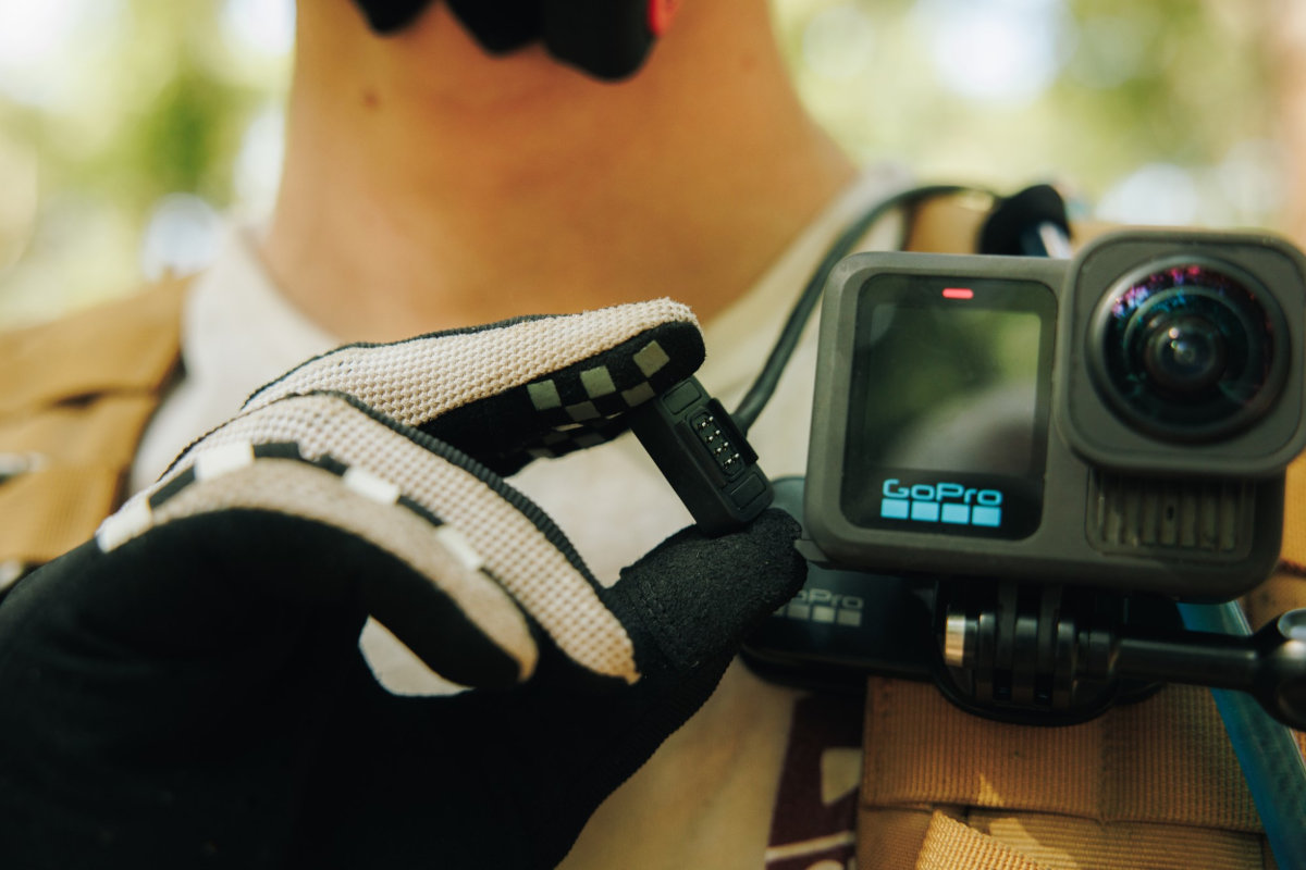 Osoba trzymająca czarną kamerę GoPro i akcesorium, zamontowane na uprzęży piersiowej.