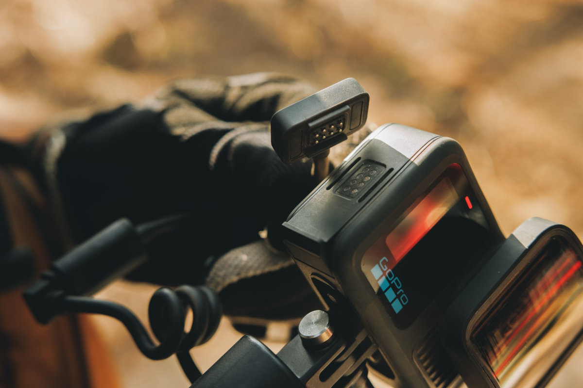 Zbliżenie kamery GoPro zamontowanej na uchwycie z dłonią w rękawicy w tle.