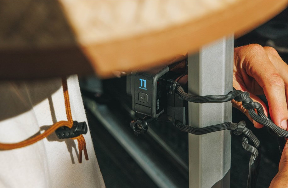 Kamera GoPro zamontowana na metalowym słupku z czarnymi paskami, regulowana przez ręce.