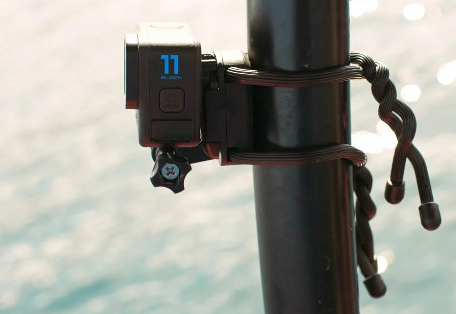Czarna kamera GoPro 11 zamontowana na czarnym słupie, z wodą w tle.