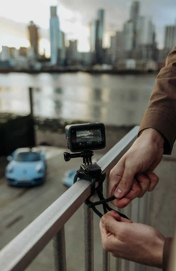 Osoba mocująca kamerę GoPro do metalowej poręczy. Panorama miasta w tle.