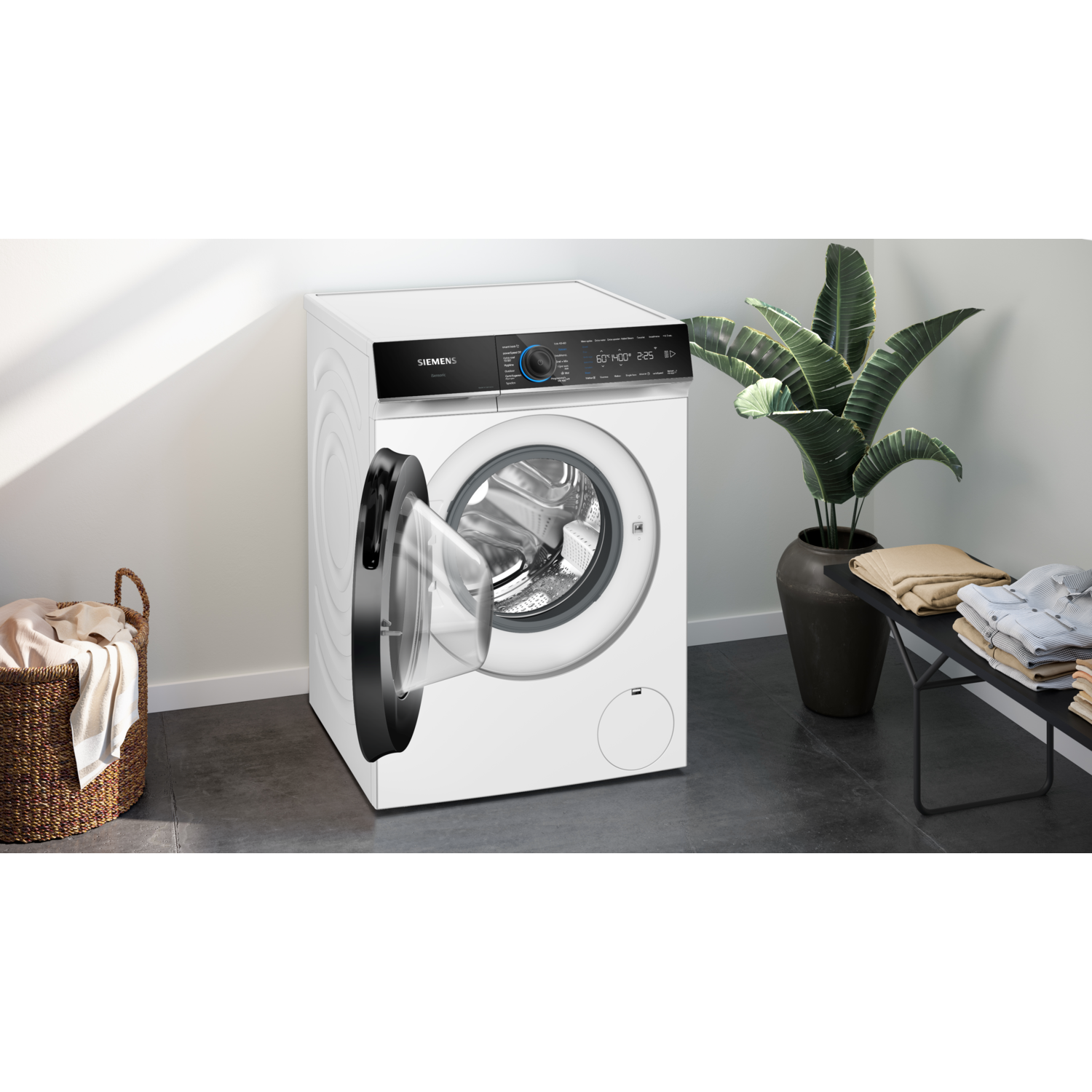 A white washing machine with an open door, basket of clothes, and a plant.