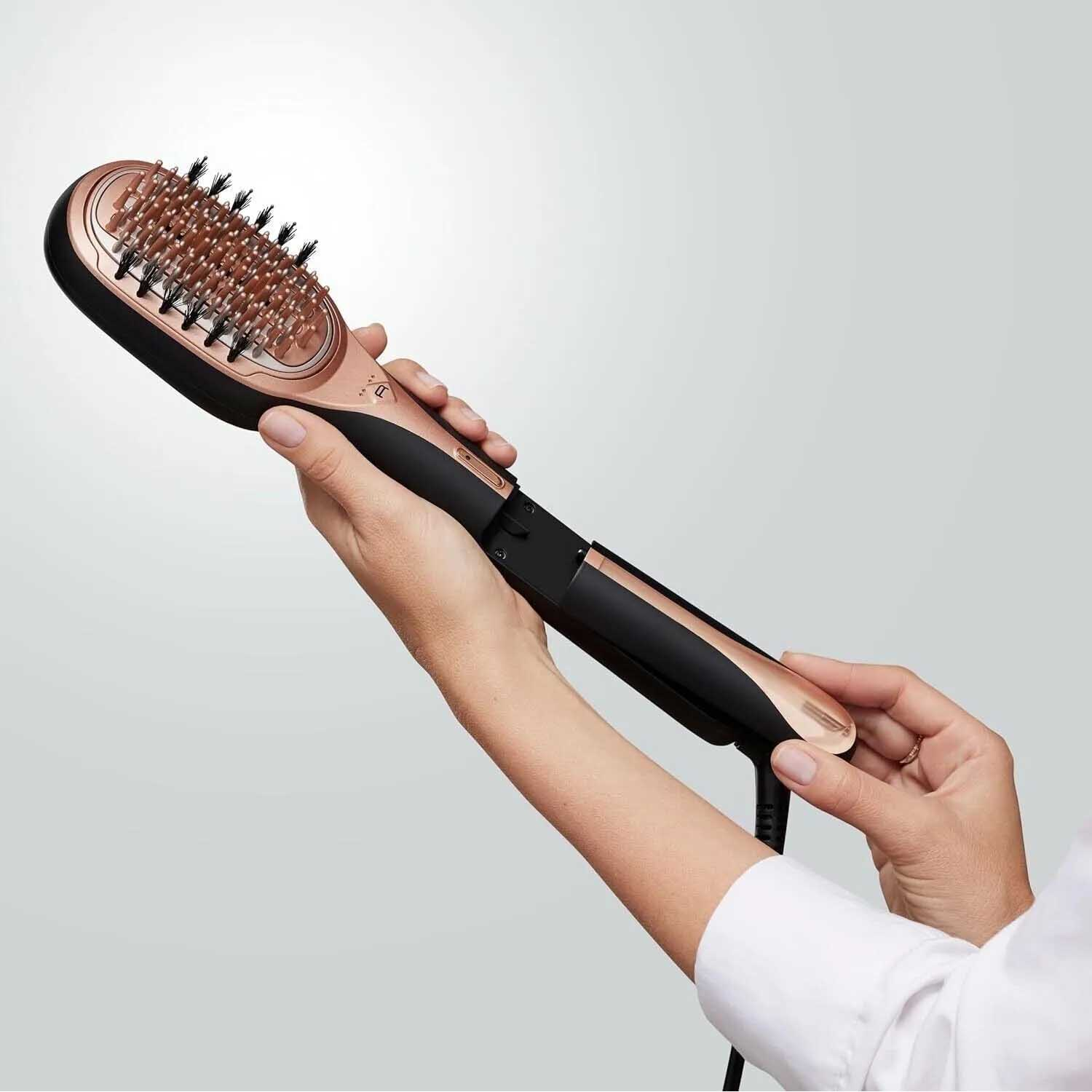 Una persona tiene in mano una spazzola lisciante per capelli nera e oro rosa. La spazzola ha setole e un cavo di alimentazione.