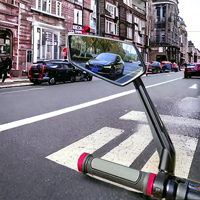 Ein Seitenspiegel eines Fahrzeugs auf einer Straße, der eine Autoreflexion und den Lenker zeigt.