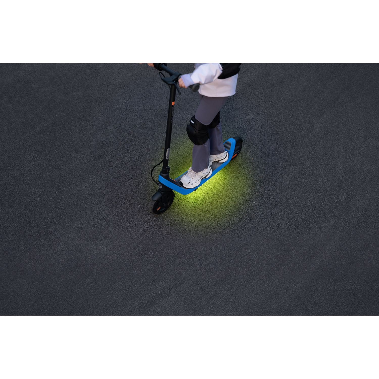 Persoon die op een blauw-zwarte scooter rijdt op een donkergrijze ondergrond. De lichten van de scooter gloeien groen.