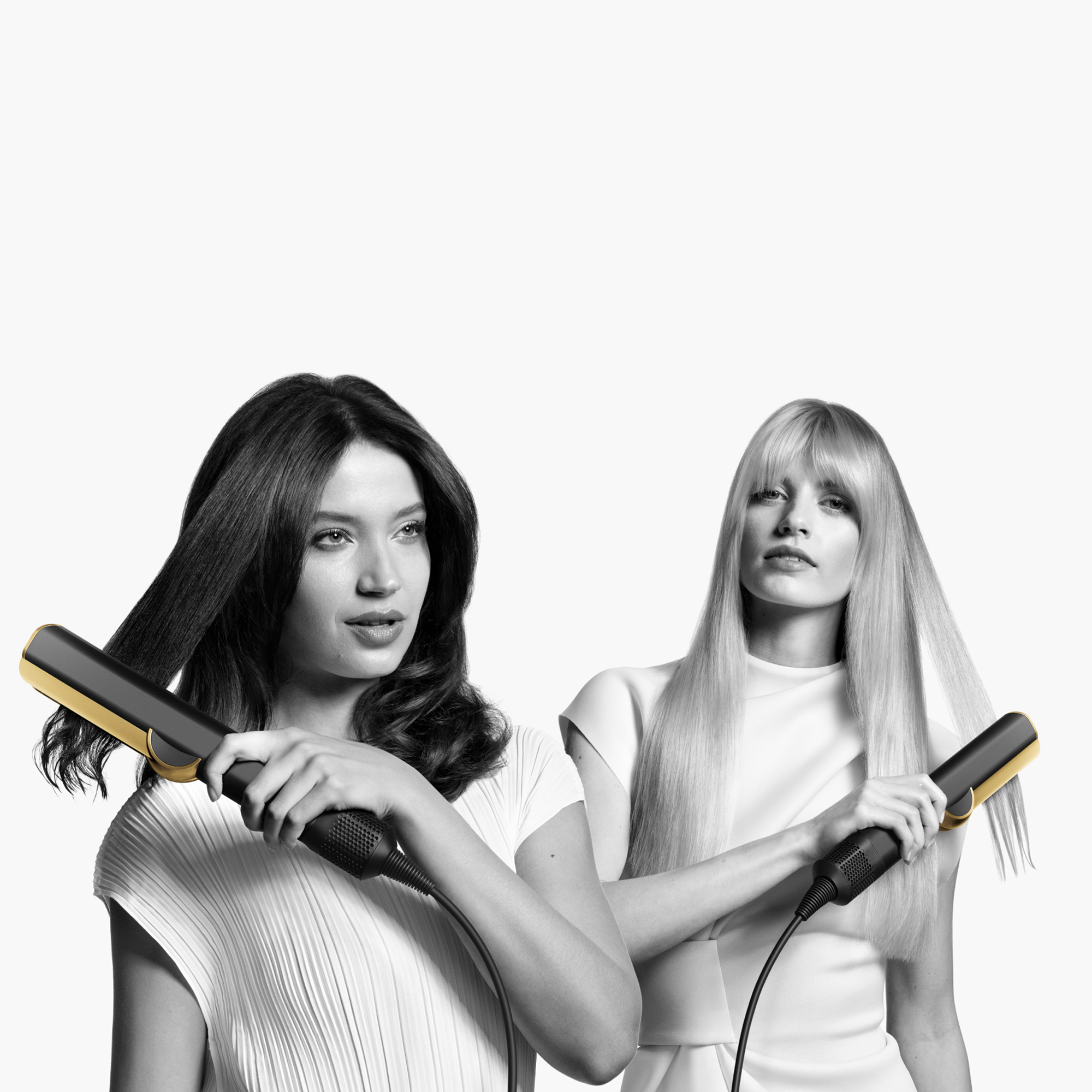 Zwei Frauen halten Haarglätter. Eine glättet dunkles Haar, die andere blondes Haar, beide vor weißem Hintergrund.
