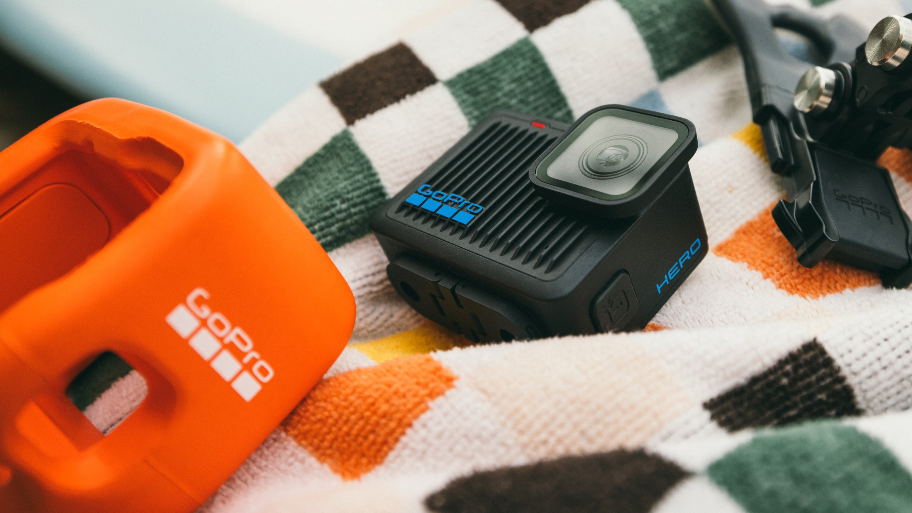 GoPro-Kamera mit Zubehör auf einem gemusterten Handtuch. Beinhaltet ein orangefarbenes Gehäuse.