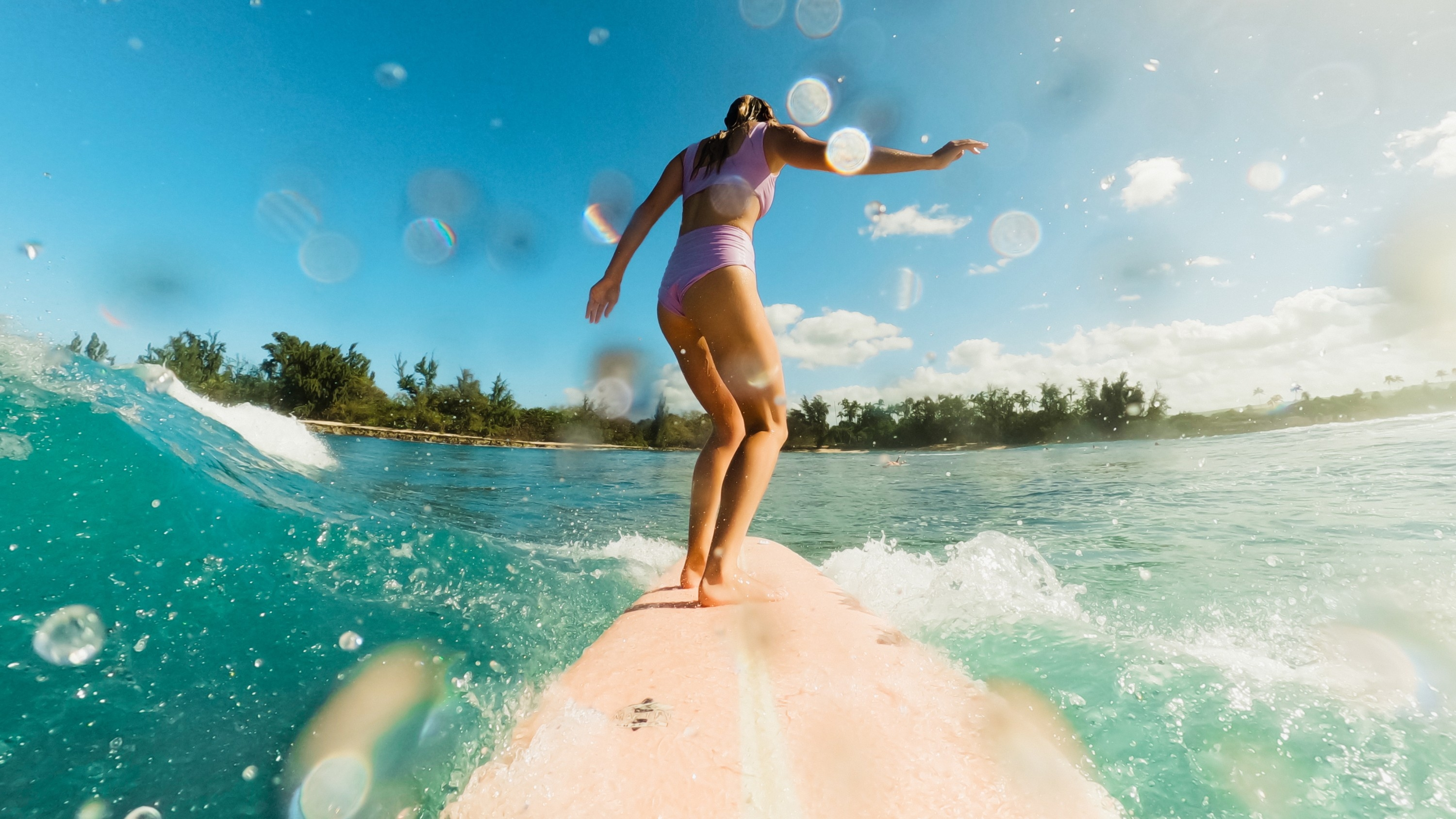 Frau surft auf einem pinken Surfbrett in Meereswellen unter blauem Himmel.