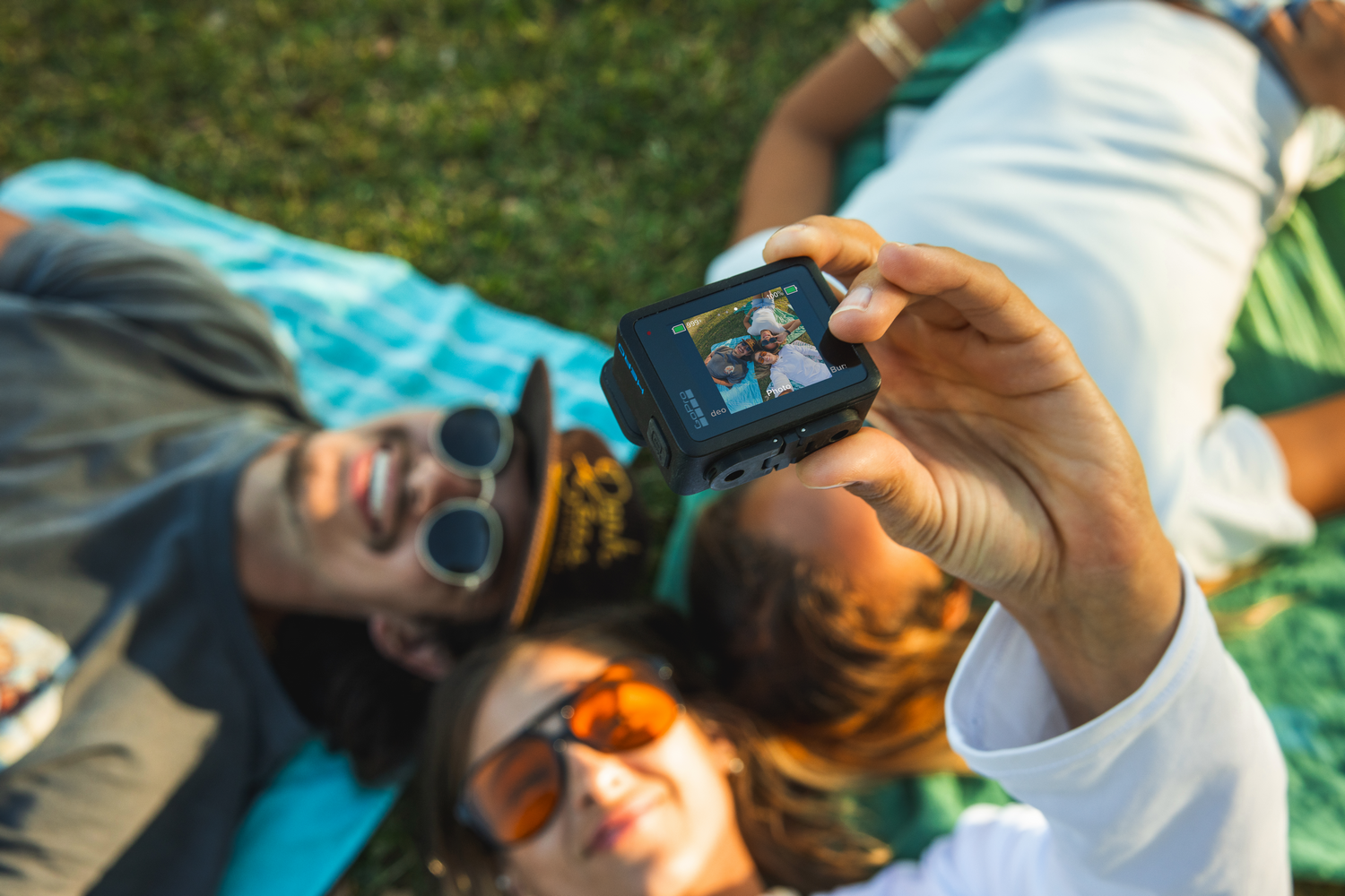 Tres personas tumbadas en la hierba, sosteniendo una cámara. La cámara muestra una selfie.
