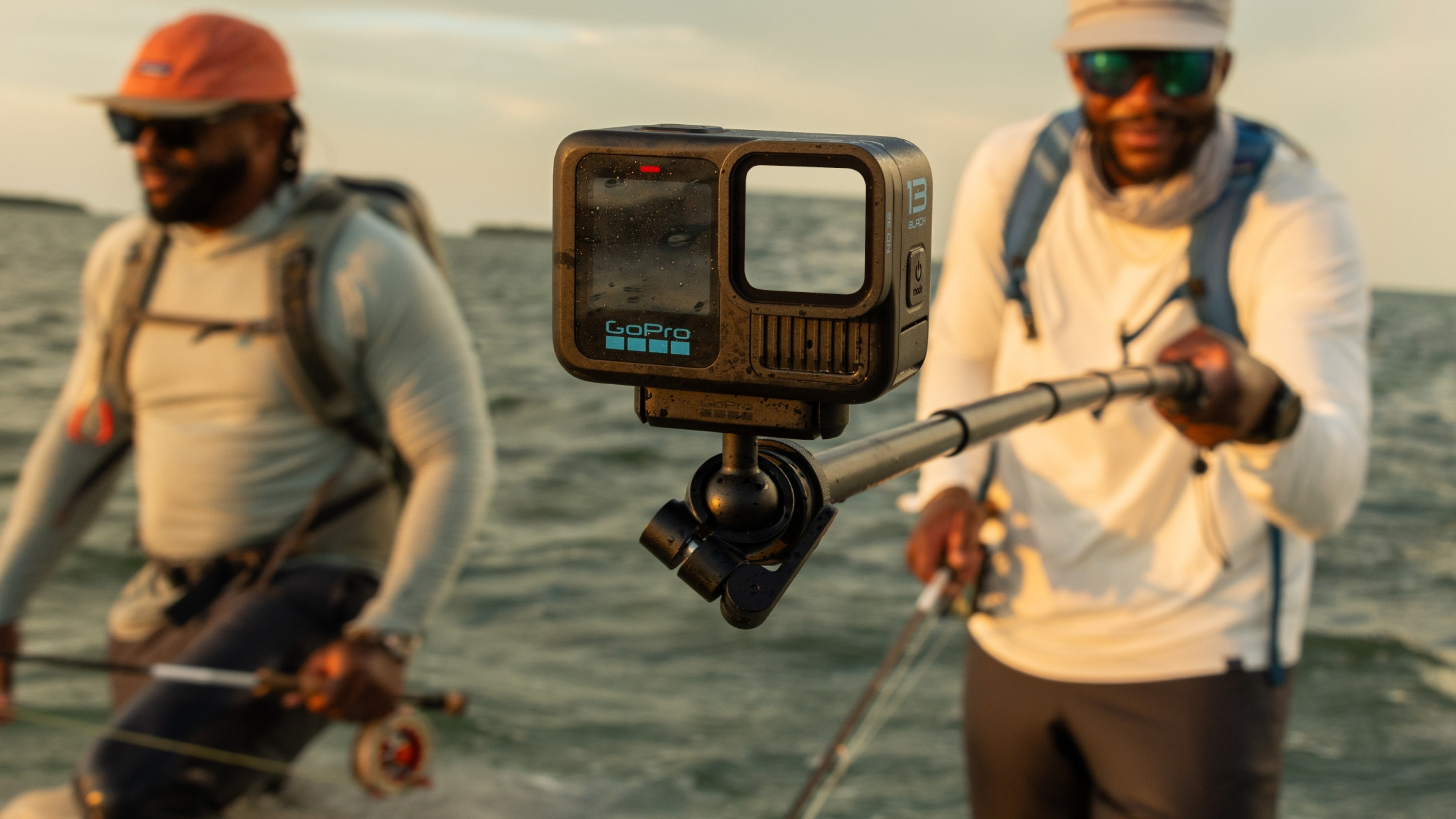 Zwei Männer, einer hält GoPro-Kamera am Stab, angeln im Wasser, sonniger Hintergrund.
