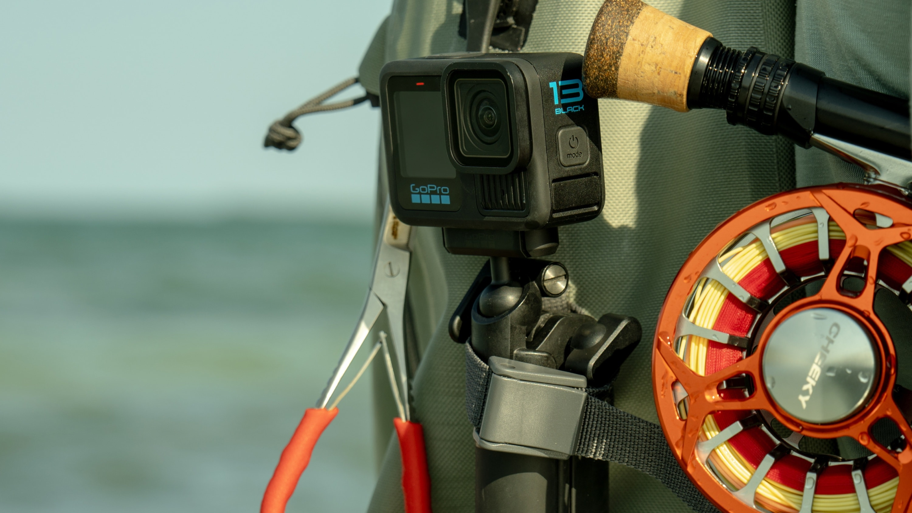 Eine GoPro-Kamera, die an einem Rucksack befestigt ist, mit Angelausrüstung im Hintergrund.
