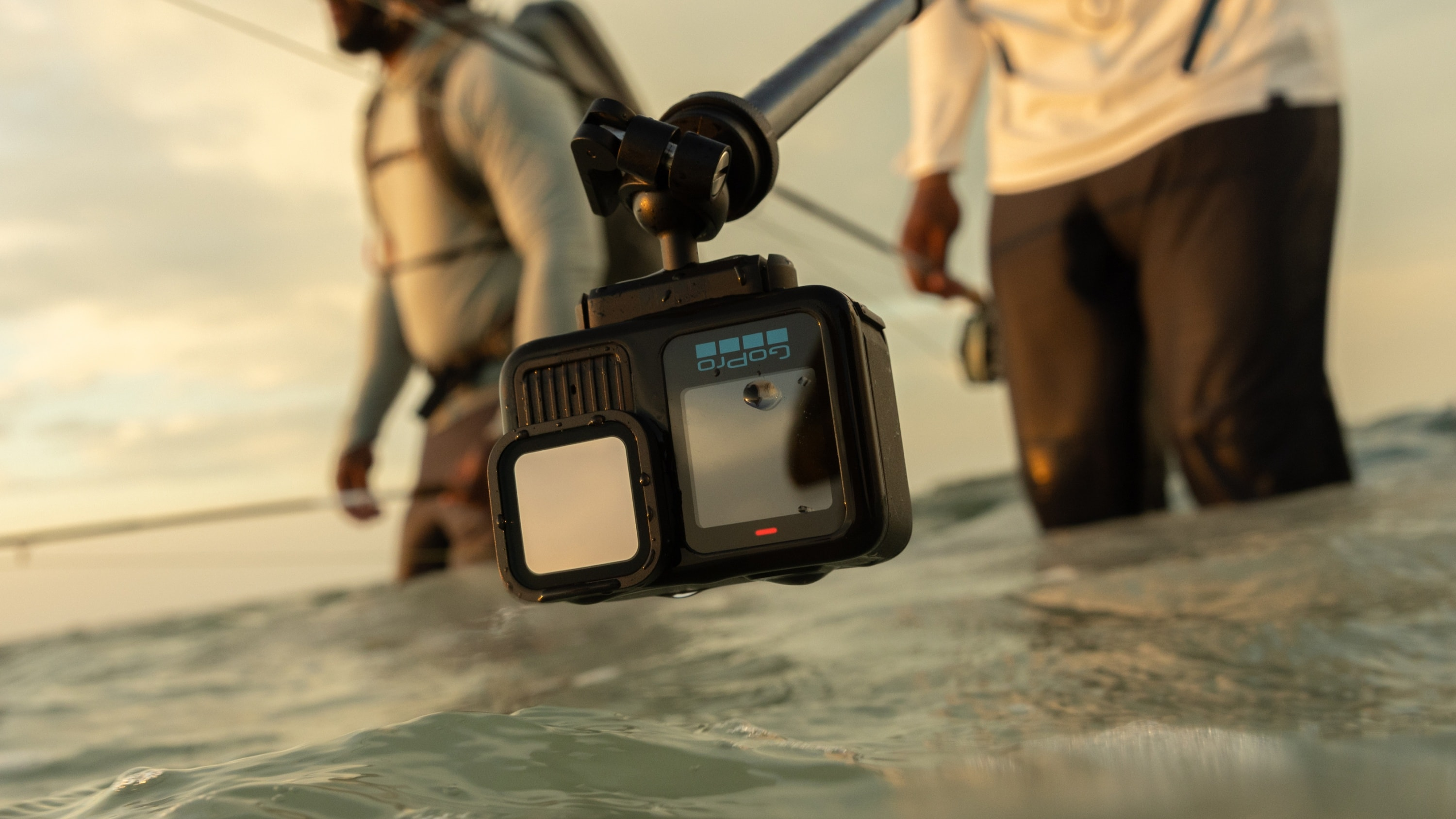 GoPro-Kamera auf einem Stab im Wasser. Zwei Personen waten im Hintergrund.