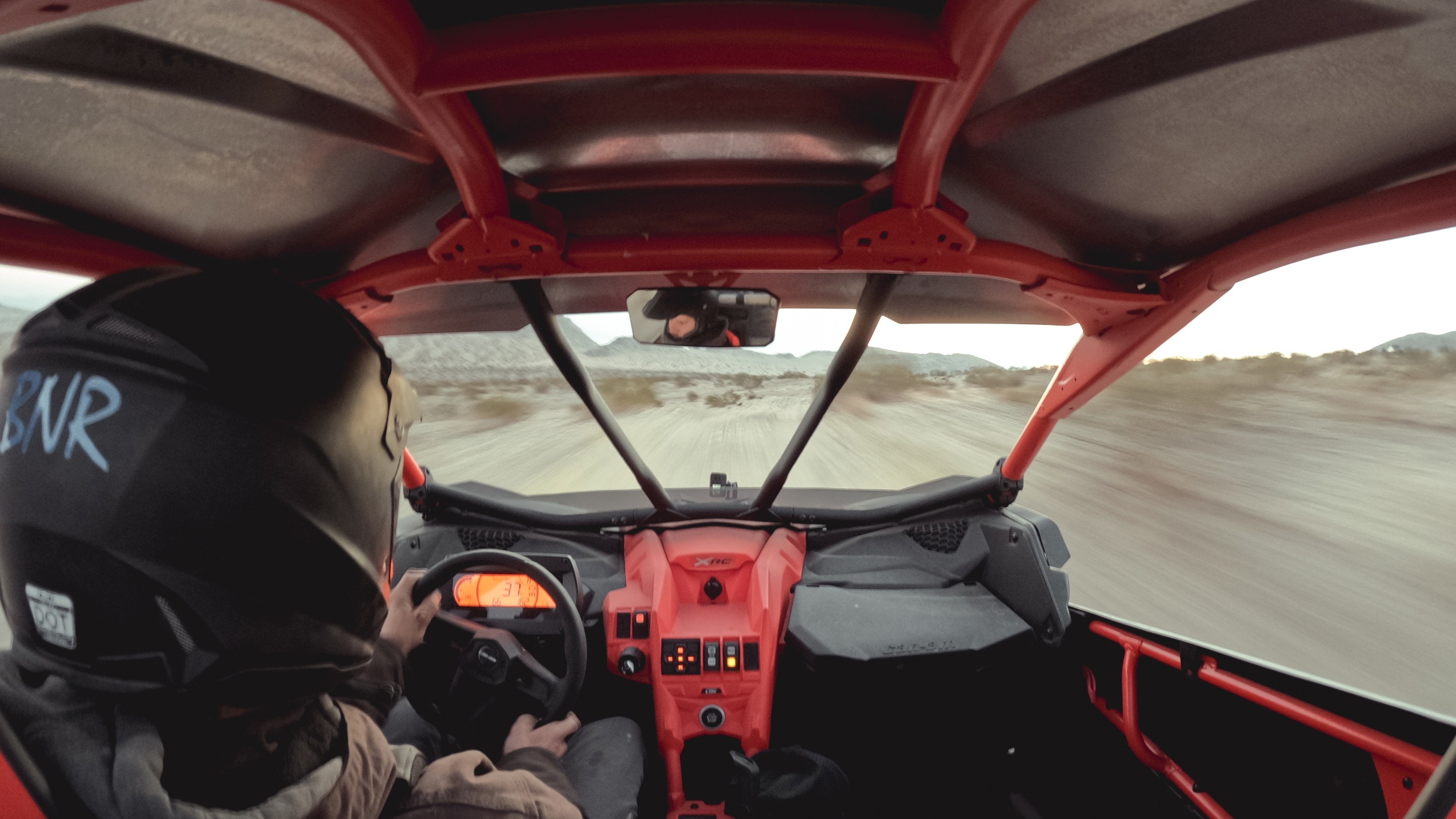 Fahrer in einem roten Buggy auf einer unbefestigten Straße. Die Ansicht ist von innen, nach vorne gerichtet.