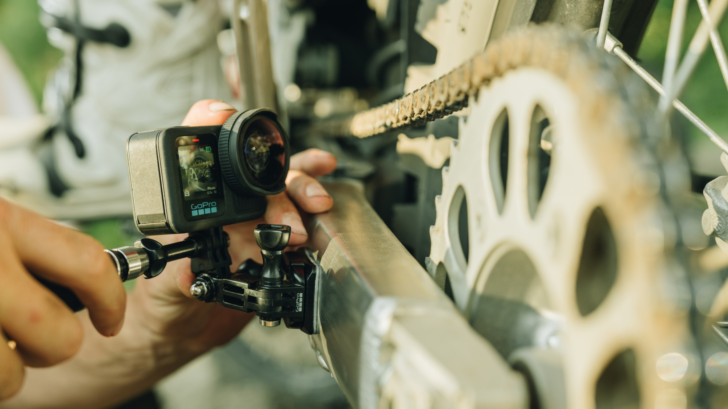 Eine GoPro-Kamera an einem Motorrad montiert. Eine Hand justiert die Kamera in der Nähe der Kette.