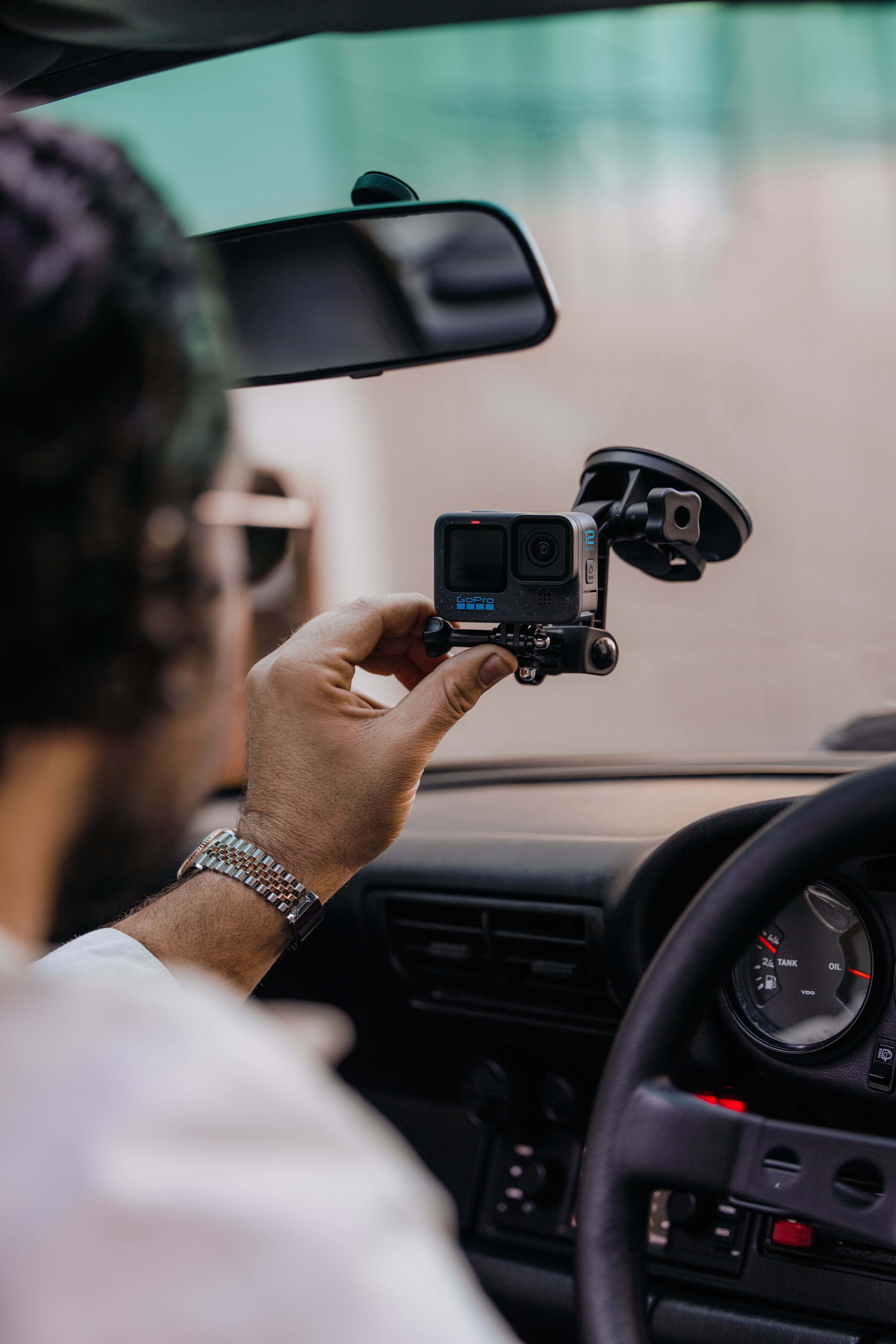 Un homme tient une caméra GoPro dans une voiture. Le tableau de bord, le volant et un rétroviseur sont visibles.