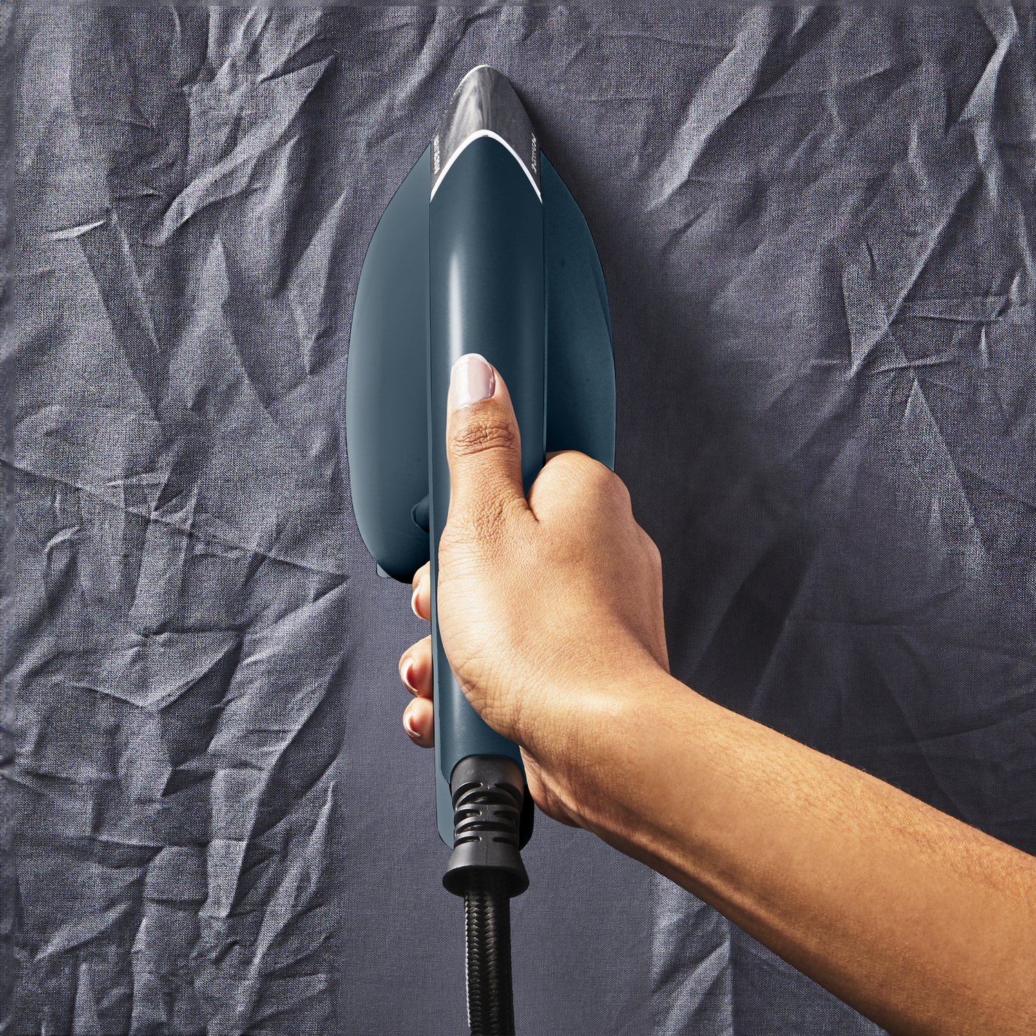 Hand holding a dark blue iron, ironing gray fabric. View from above.