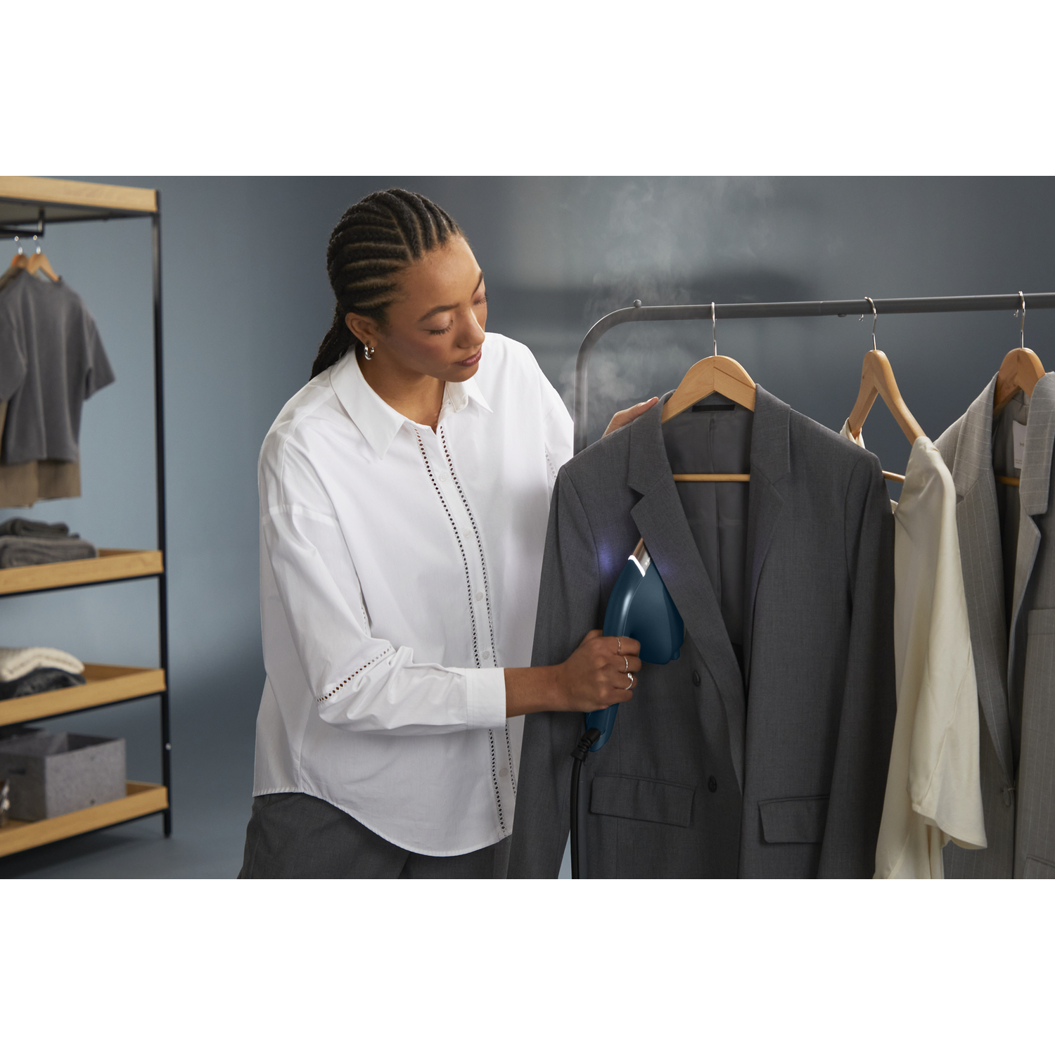 Woman steaming a gray suit jacket on a clothing rack.