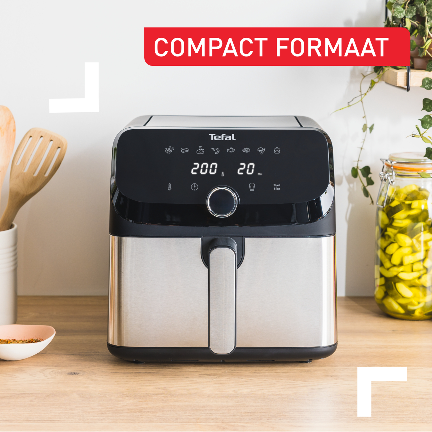 A Tefal air fryer on a wooden surface, with jars and utensils.